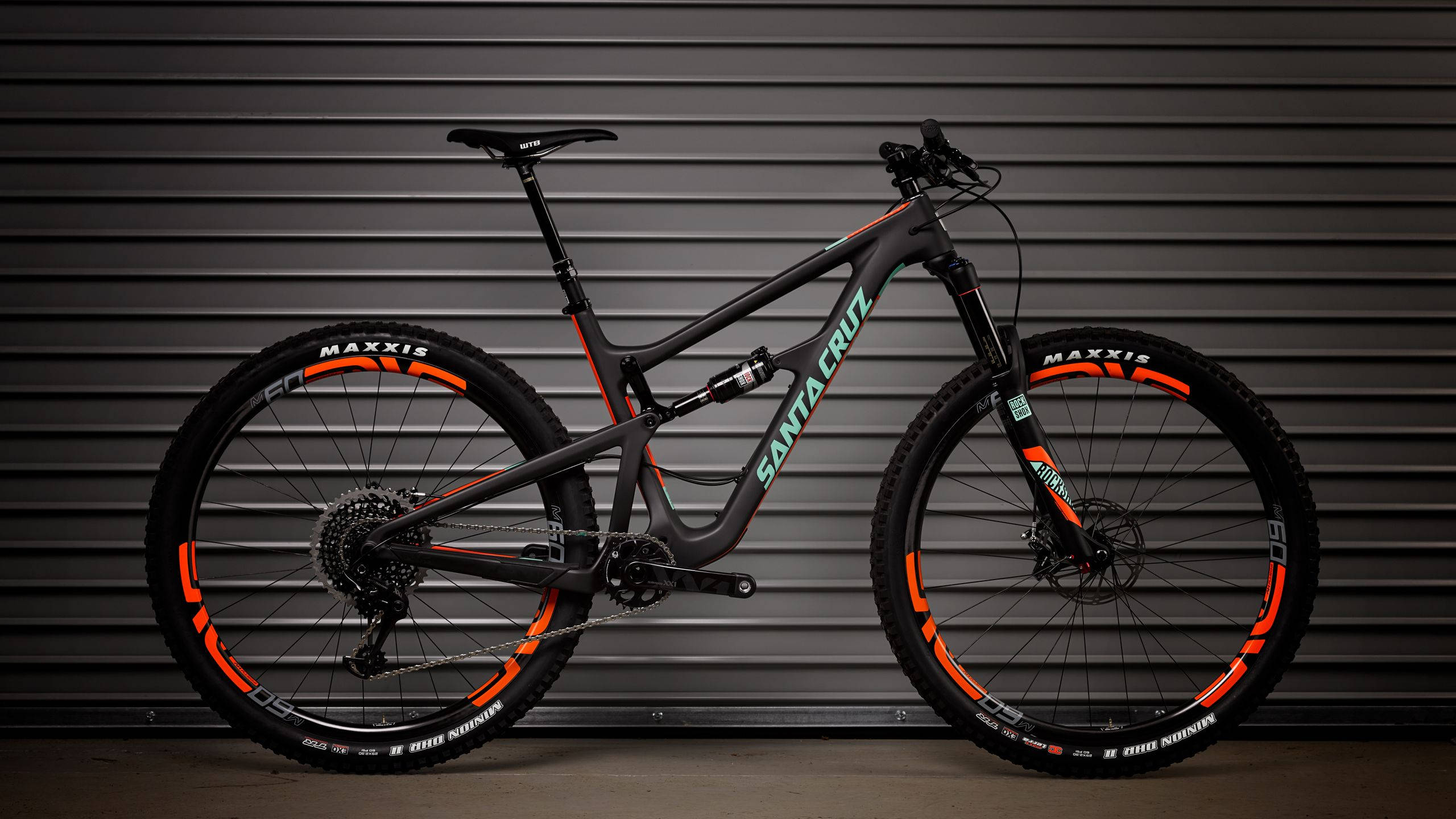 Mountain Bike 桌布 壁紙 — 一台時尚的黑橙色Santa Cruz登山車，矗立在深灰色波紋金屬背景前。