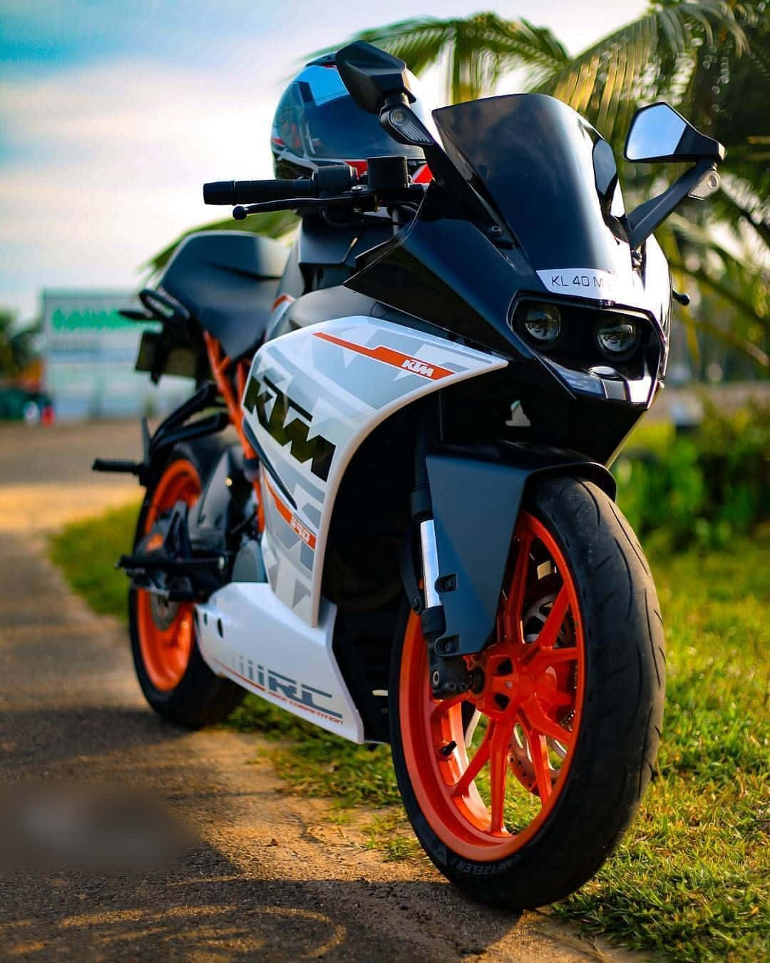 機車 桌布 壁紙 — 一台時尚的黑白KTM機車，配以鮮豔的橙色車輪，停放在晴朗天空下的草地路邊。