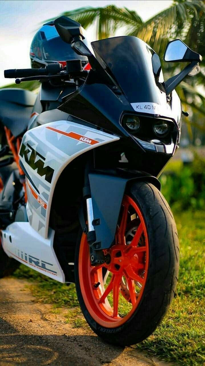 KTM RC 200 桌布 壁紙 — 一台時尚的黑白KTM機車，配以鮮豔的橙色輪胎，停泊在棕櫚樹下的草地上。