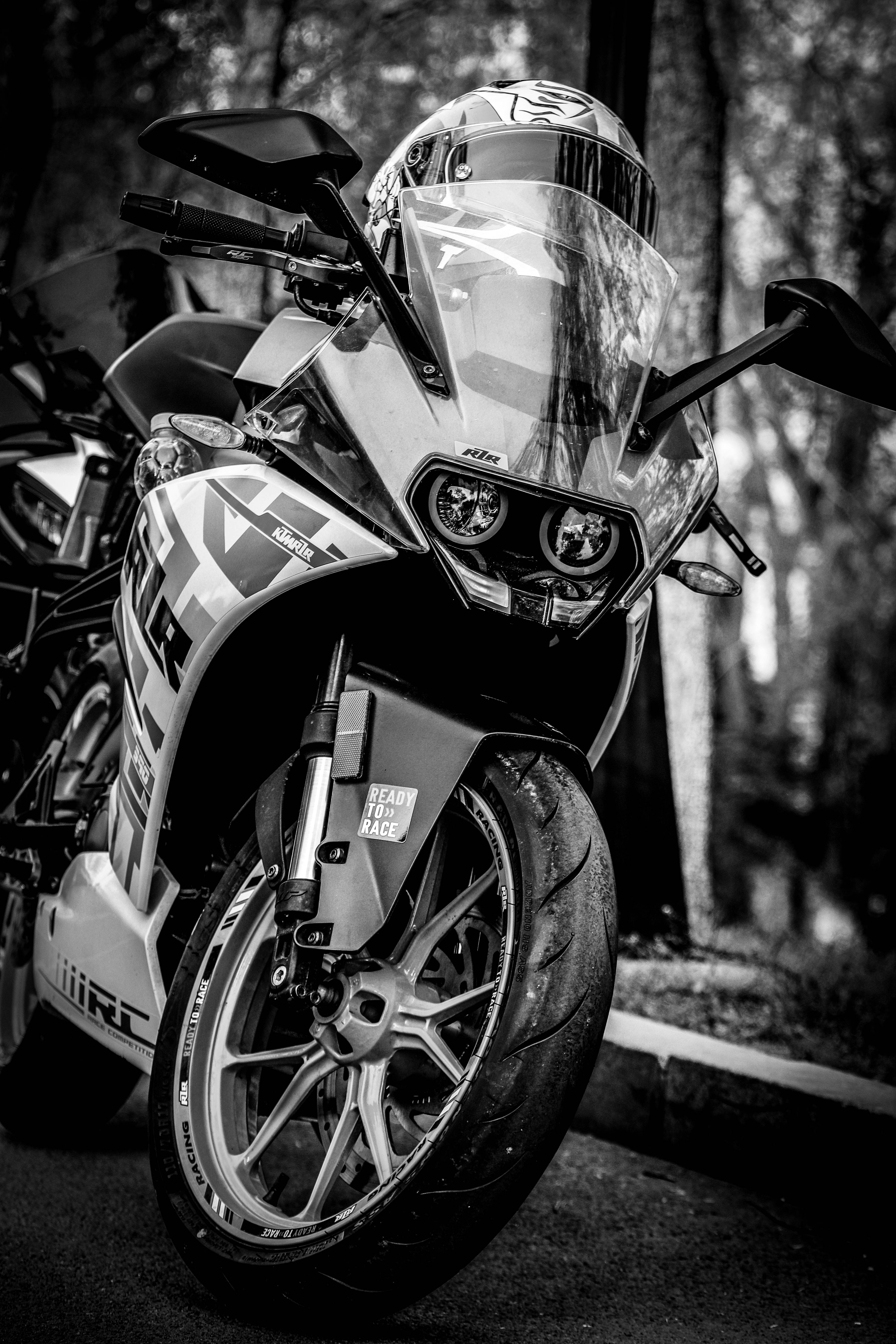 Ktm Rc 390 桌布 壁紙 — 一台時尚的黑白運動機車，安全帽擱在擋風玻璃上，停放在樹林地區。