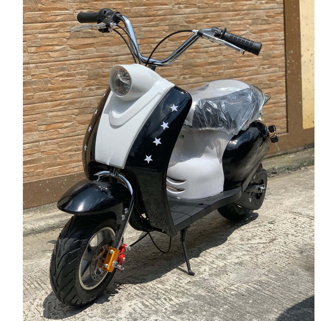 scooter 桌布 壁紙 — 一台時尚的黑白電動滑板車，帶有星星貼紙，停在混凝土人行道上，靠著磚牆，在明亮的陽光下。