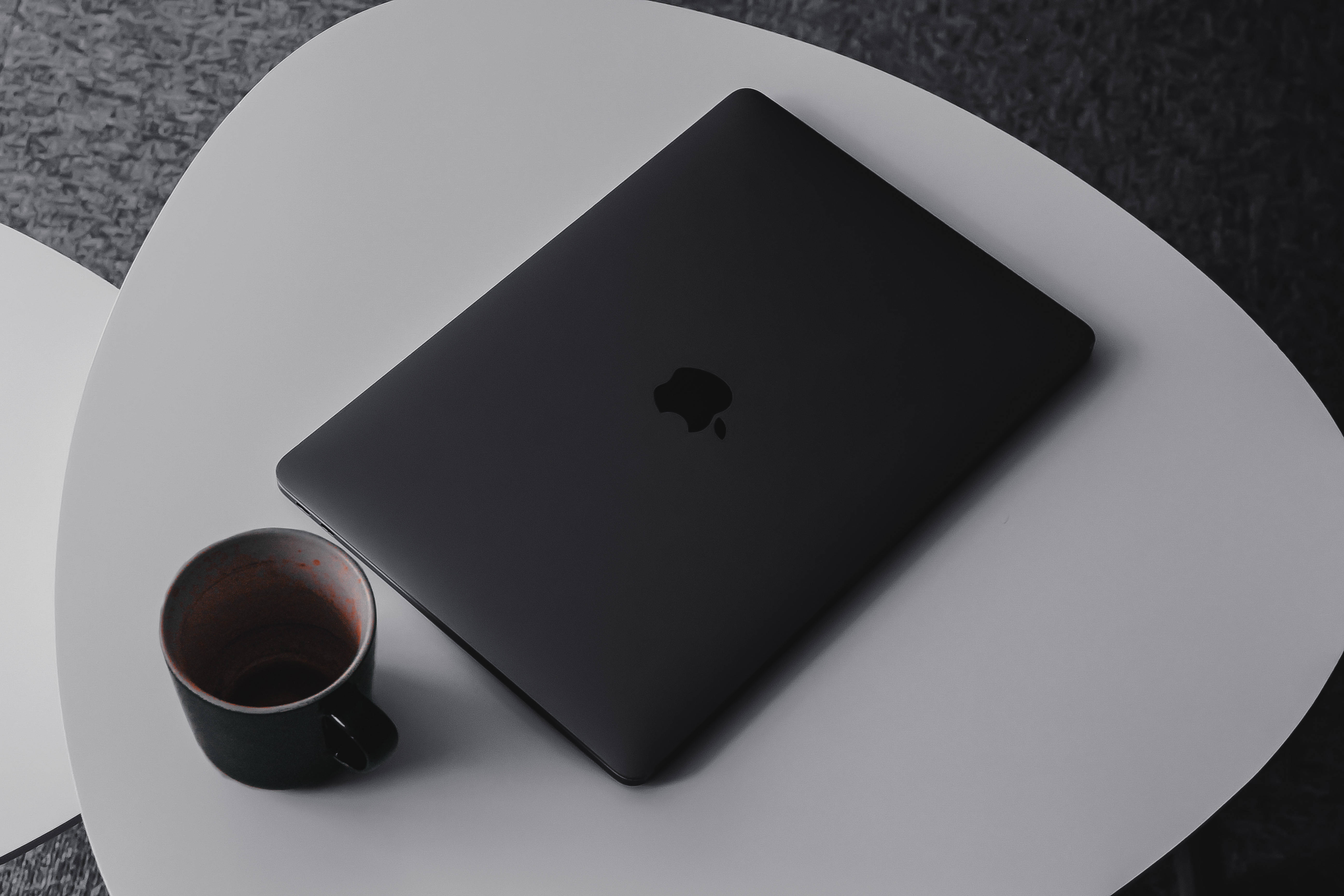 MacBook 動態圖片 桌布 壁紙 — 一台時尚的黑色 MacBook 放在一張簡約白色桌子上，旁邊有一個空的咖啡杯。