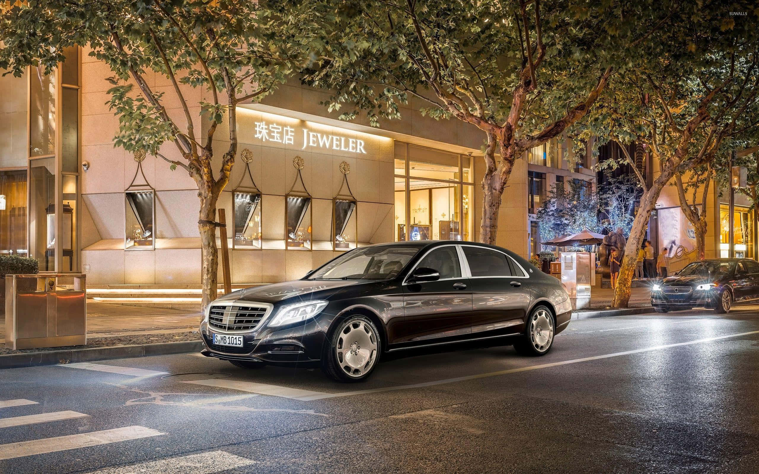 Maybach 桌布 壁紙 — 一台時尚的黑色 Mercedes-Maybach S-Class 在夜晚沿著濕漉漉的城市街道滑行，經過一間閃閃發光的珠寶店。