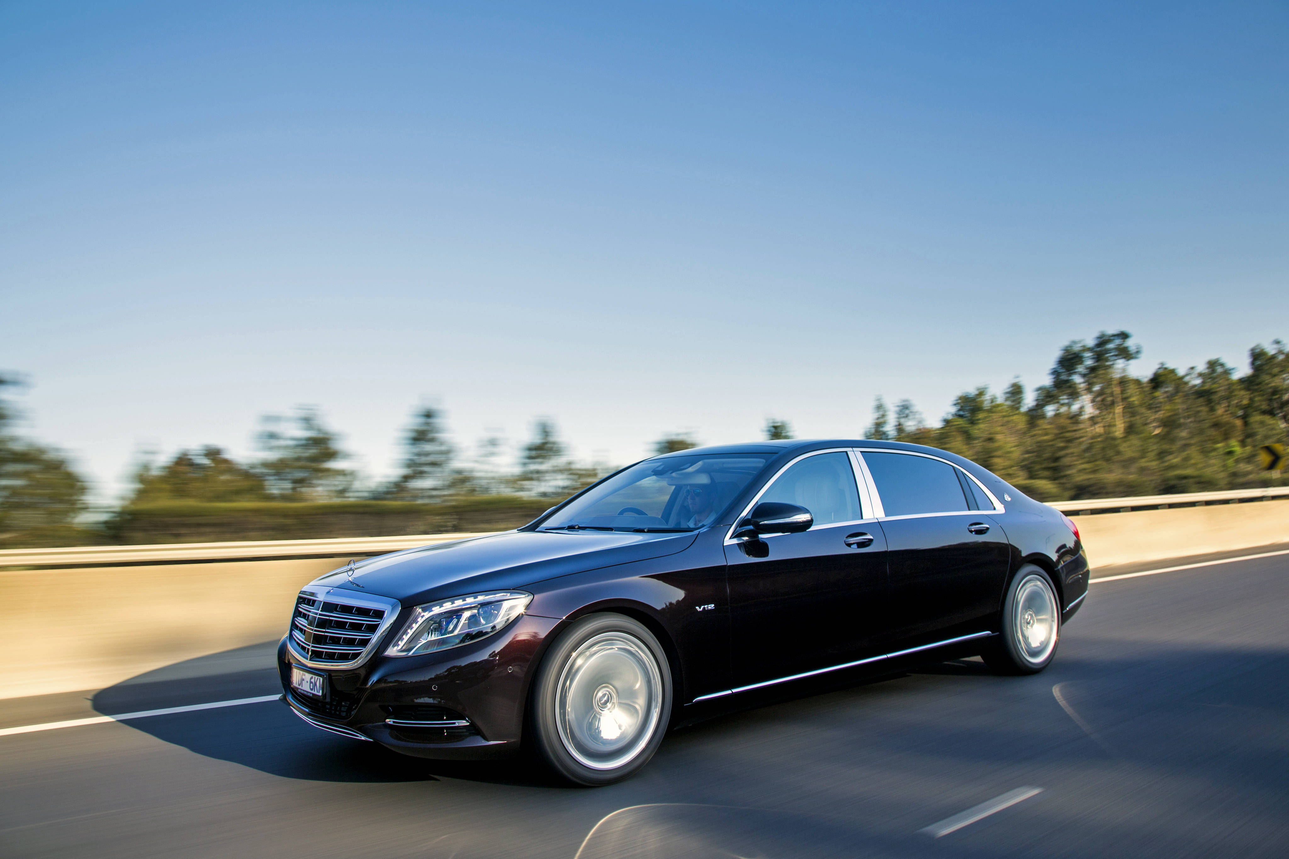 benz 4K 桌布 壁紙 — 一台時尚的黑色 Mercedes-Maybach S600 在陽光明媚的高速公路上平穩行駛，背景是模糊的綠色樹木。