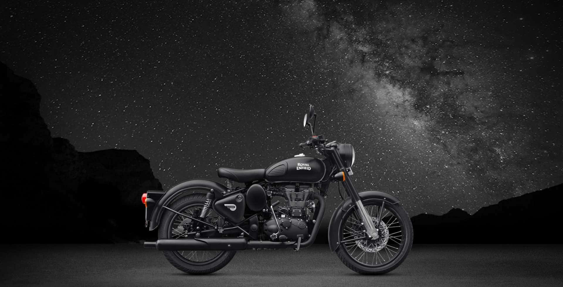 機車 桌布 壁紙 — 一台時尚的黑色 Royal Enfield 摩托車在星空下蓄勢待發，銀河在輪廓分明的山巒上方拱起。