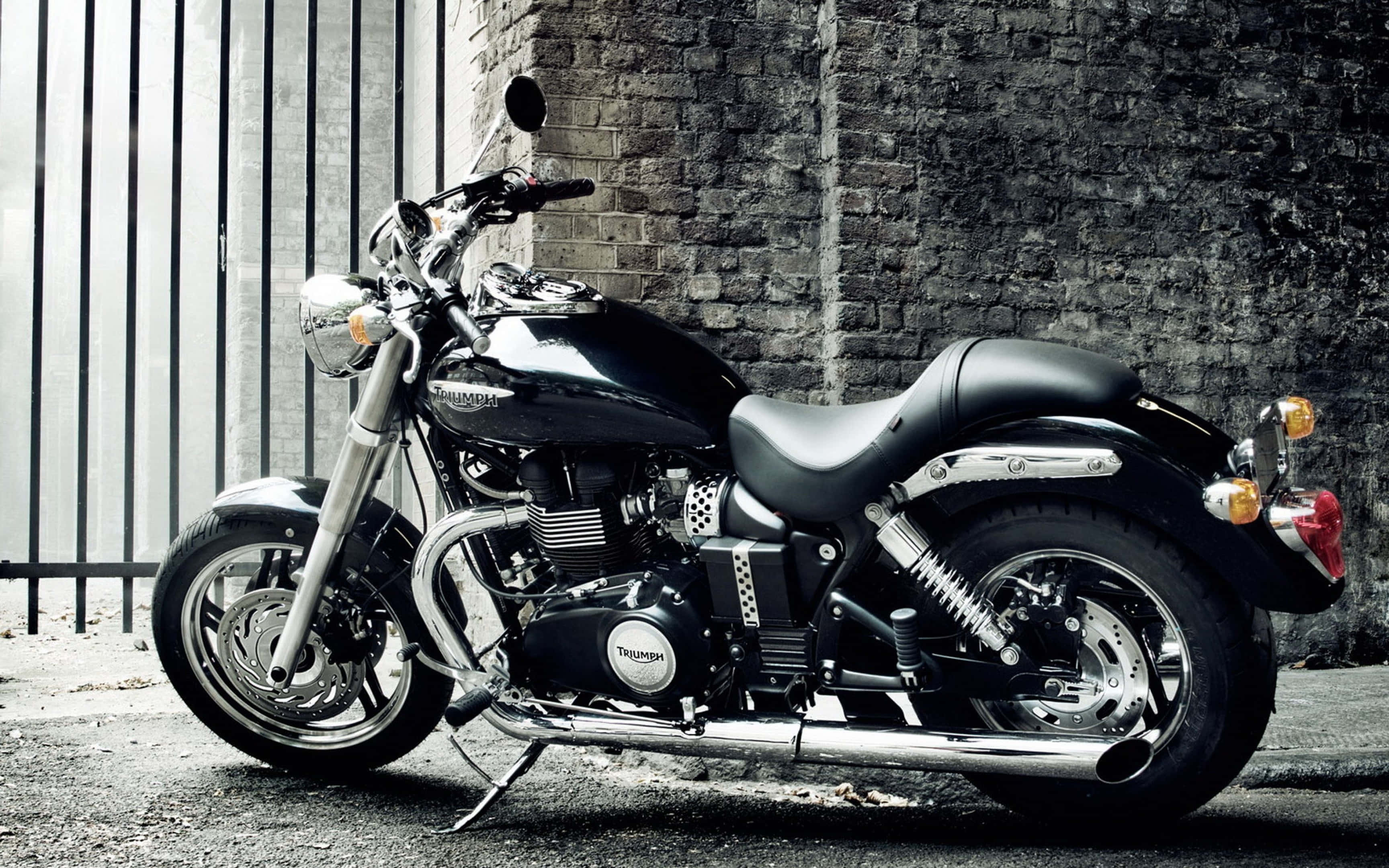 桌布 壁紙 — 一台時尚的黑色 Triumph 摩托車，帶有鍍鉻裝飾，靠在金屬圍欄旁邊的風化磚牆上。