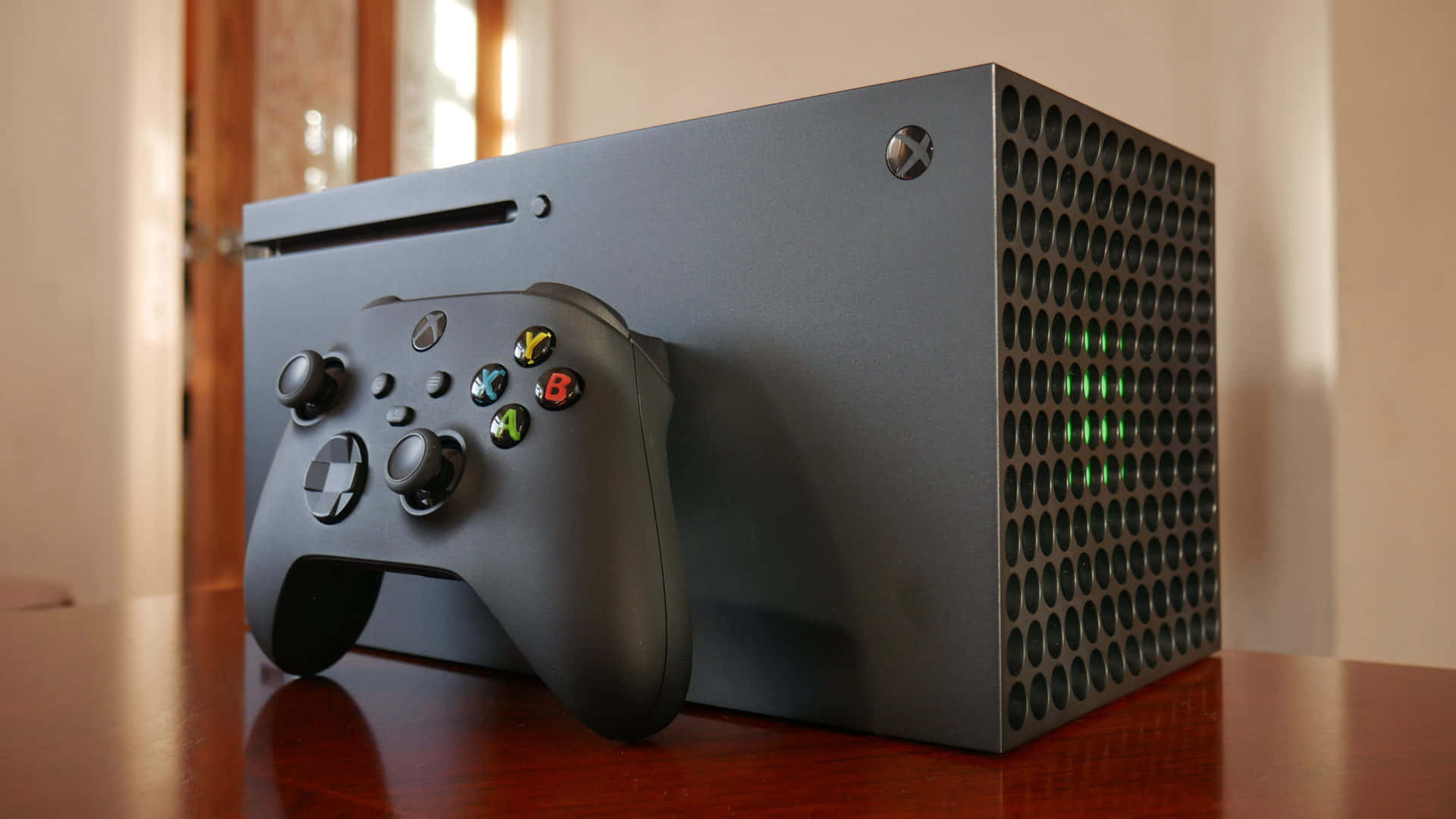Xbox 桌布 壁紙 — 一台時尚的黑色 Xbox Series X 主機，帶有發光的綠色 LED 燈，與其匹配的控制器一起放在拋光木桌上。