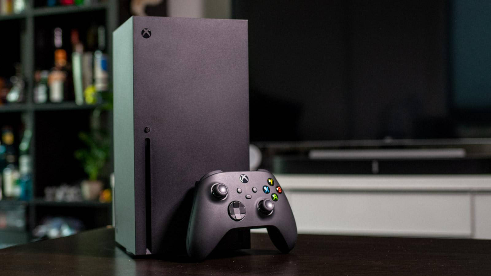 Xbox 桌布 壁紙 — 一台時尚的黑色 Xbox Series X 主機和手把放在舒適客廳的深色木桌上。