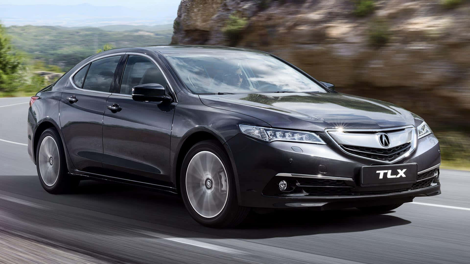 Acura Tlx 桌布 壁紙 — 一台時尚的黑色Acura TLX轎車沿著蜿蜒的山路疾馳，背景是模糊的綠色山丘和岩石峭壁。