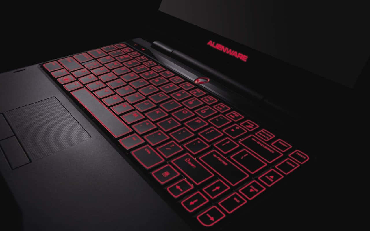 背景 桌布 壁紙 — 一台時尚的黑色Alienware筆記型電腦，帶有紅色背光按鍵和標誌，在黑暗背景下發光。