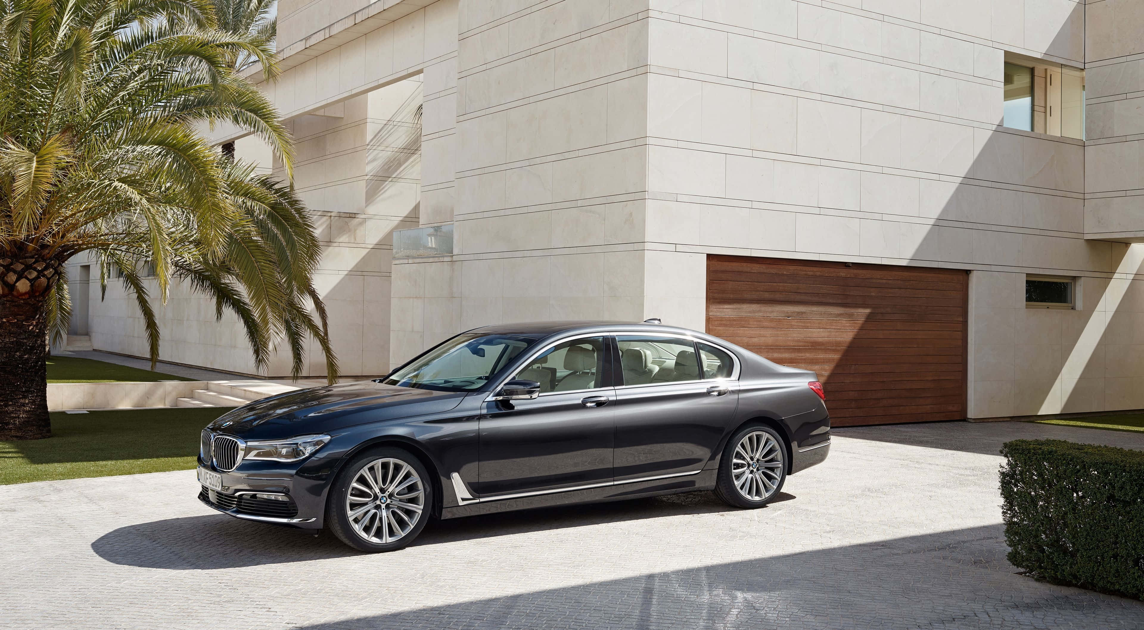Bmw 7 Series 桌布 壁紙 — 一台時尚的黑色BMW 7系列轎車停放在陽光普照的車道上，旁邊是一座現代住宅和一棵棕櫚樹。