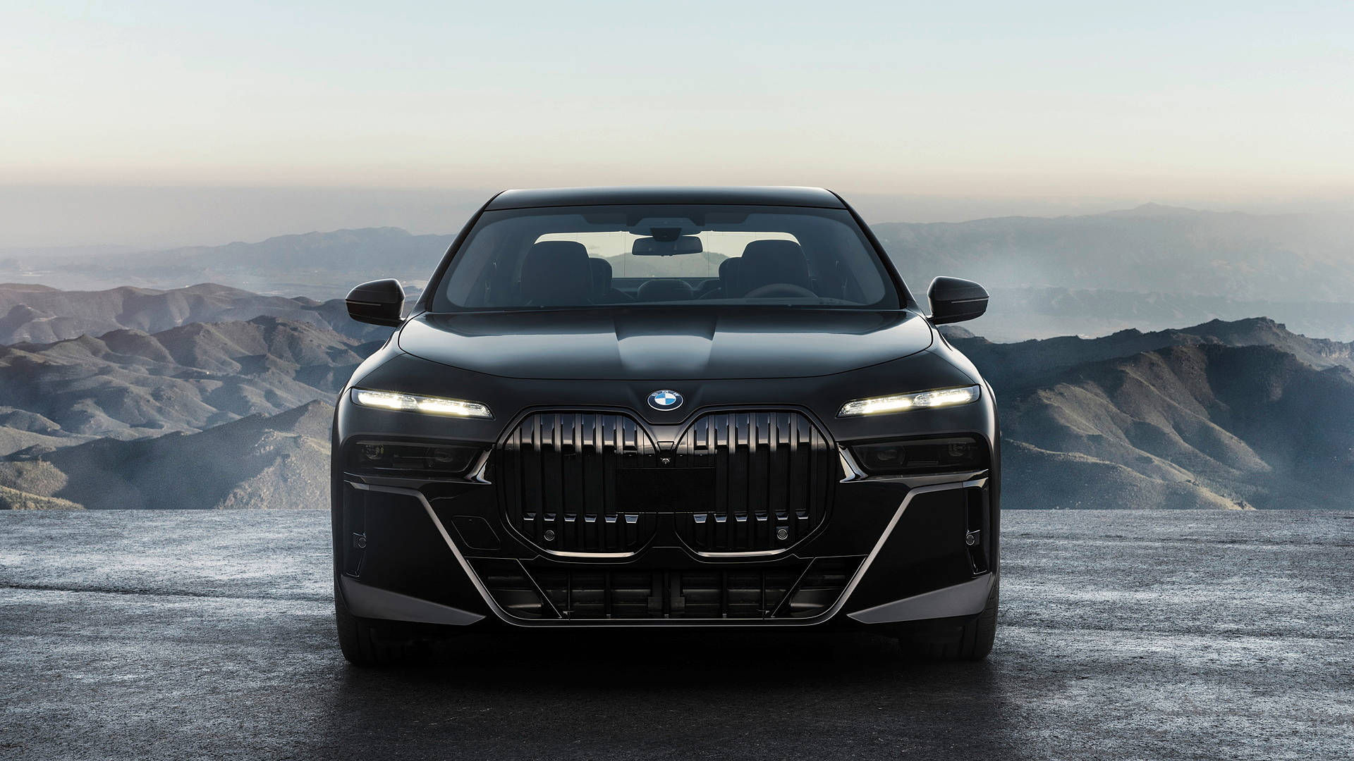 Outdoor 桌布 壁紙 — 一台時尚的黑色BMW i7電動轎車在懸崖邊緣向前，俯瞰黎明時分霧氣繚繞的山脈。