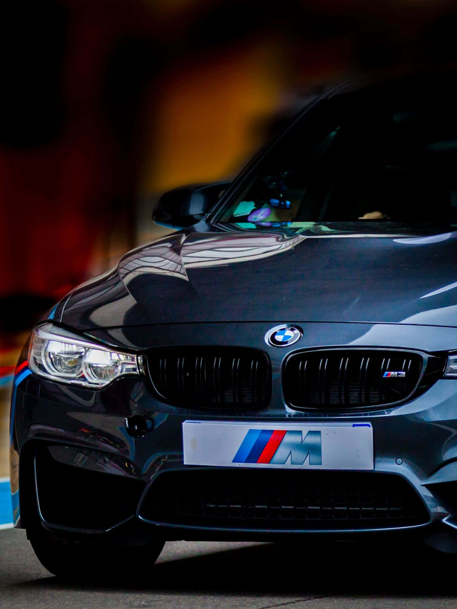 BMW 動圖 桌布 壁紙 — 一台時尚的黑色BMW M3跑車在戲劇性燈光下閃閃發光，背景是模糊的火光。