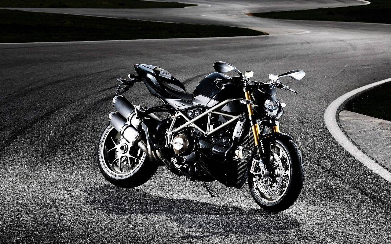 機車 桌布 壁紙 — 一台時尚的黑色Ducati摩托車配金色前叉，夜晚停在空無一人的柏油路上，在戲劇性的燈光下投射出銳利的陰影。