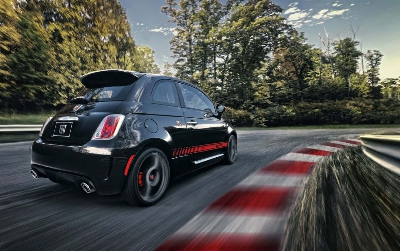 Fiat 500l 桌布 壁紙 — 一台時尚的黑色Fiat 500 Abarth在蜿蜒的森林道路上疾馳，紅白條紋護欄模糊掠過。