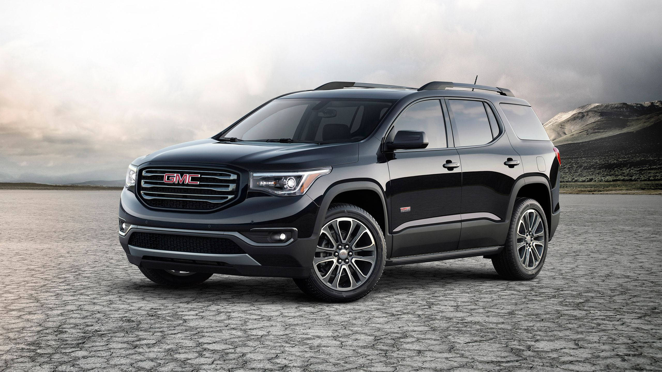 Gmc 桌布 壁紙 — 一台時尚的黑色GMC Acadia SUV停放在龜裂的沙漠地面上，天空多雲，遠山在望。