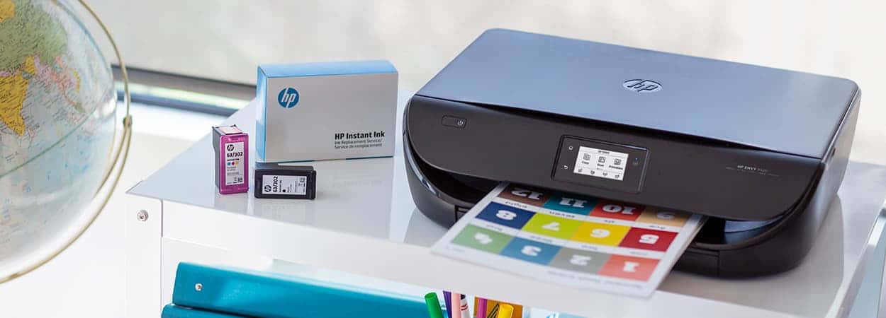 Printer 桌布 壁紙 — 一台時尚的黑色HP印表機在白色桌子上，旁邊有地球儀和墨水匣，列印出一張彩色紙張。