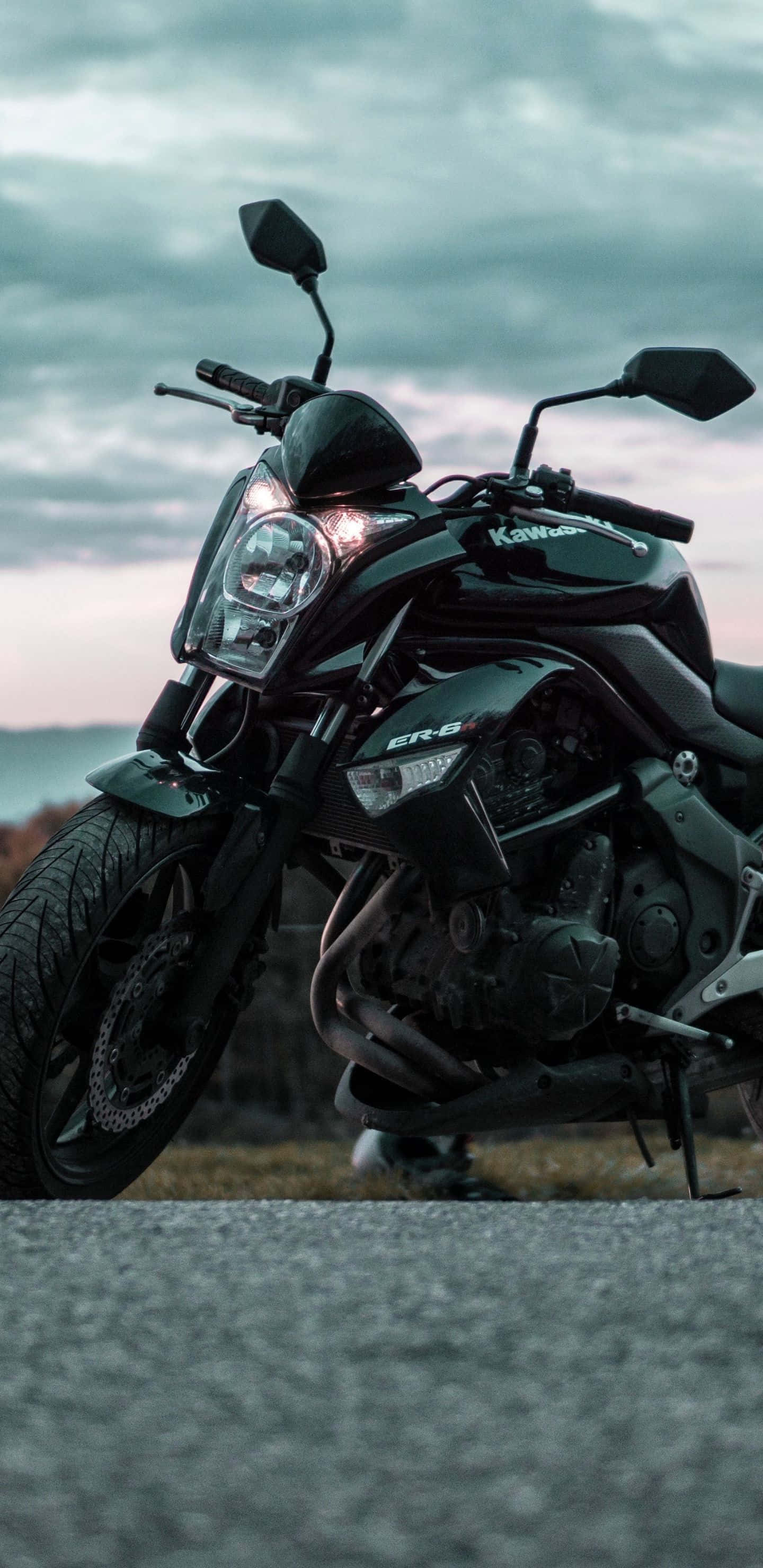 Pixel 3xl Bikes 桌布 壁紙 — 一台時尚的黑色Kawasaki ER-6摩托車停在碎石路上，背景是帶有柔和粉紅與灰色雲層的憂鬱暮色天空。