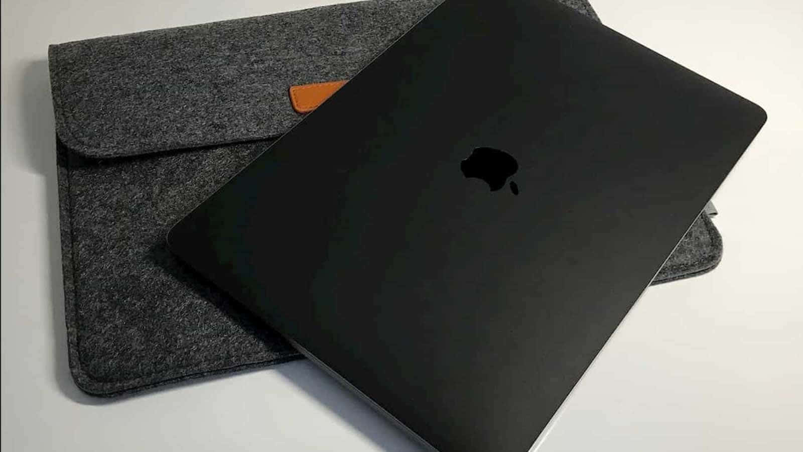 Black Macbook 桌布 壁紙 — 一台時尚的黑色MacBook放在灰色氈套上，帶有橙色皮革點綴，置於潔白表面上。