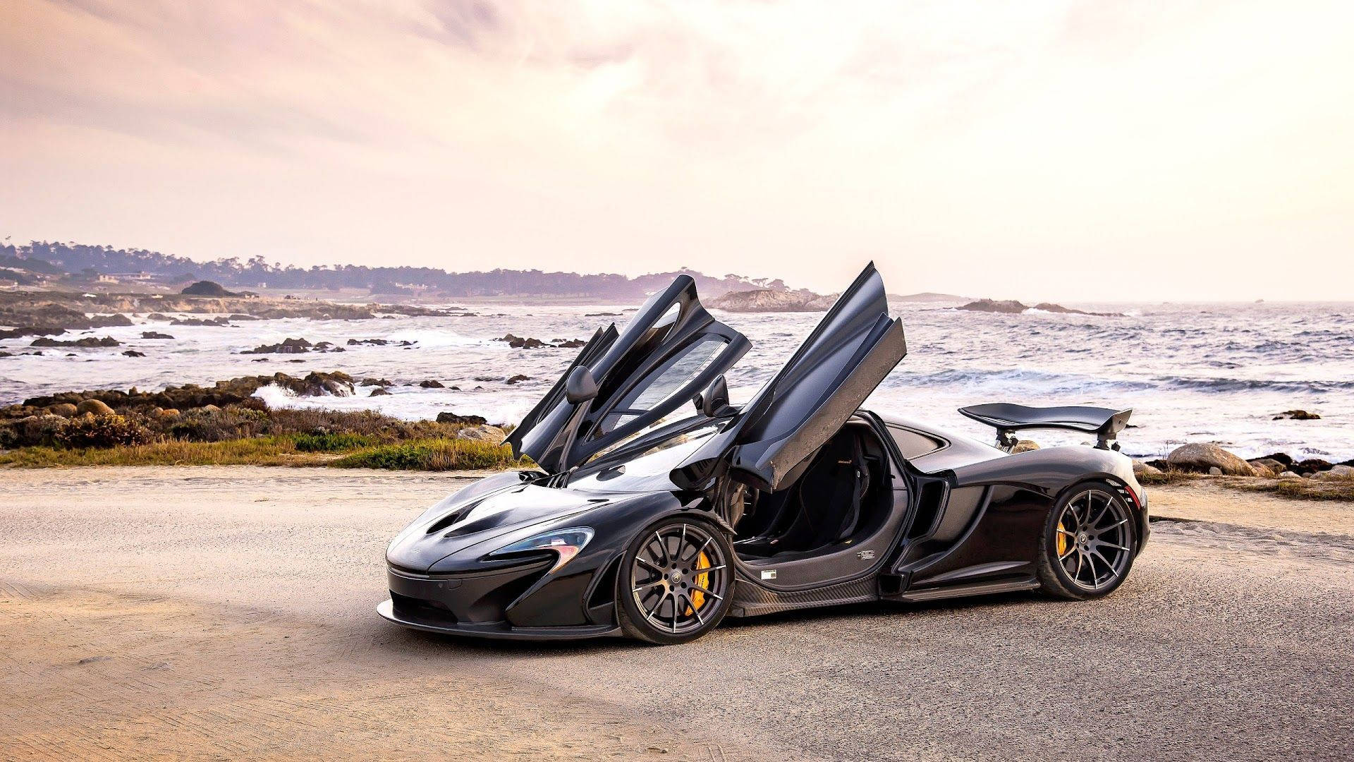 麥拉倫 桌布 壁紙 — 一台時尚的黑色McLaren跑車，蝴蝶門打開，停在日落時分的海岸公路上。