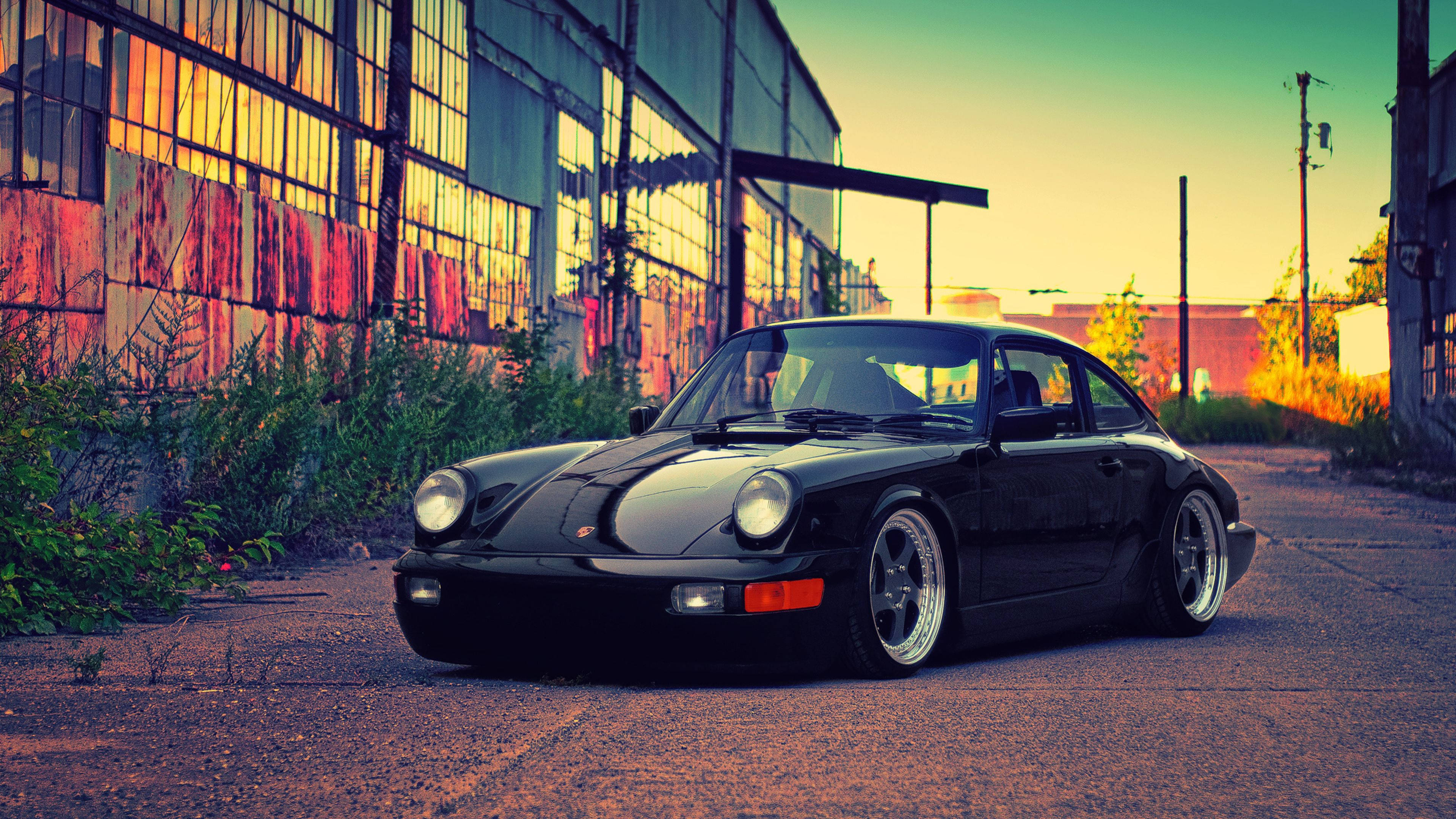 Porsche 911 桌布 壁紙 — 一台時尚的黑色保時捷911在日落時分停泊在佈滿灰塵的城市街道上，在風化的工業建築上投下長長的影子。