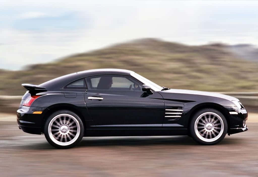 Chrysler Crossfire 桌布 壁紙 — 一台時尚的黑色克萊斯勒 Crossfire 跑車在沙漠公路上奔馳，背景是模糊的山丘。
