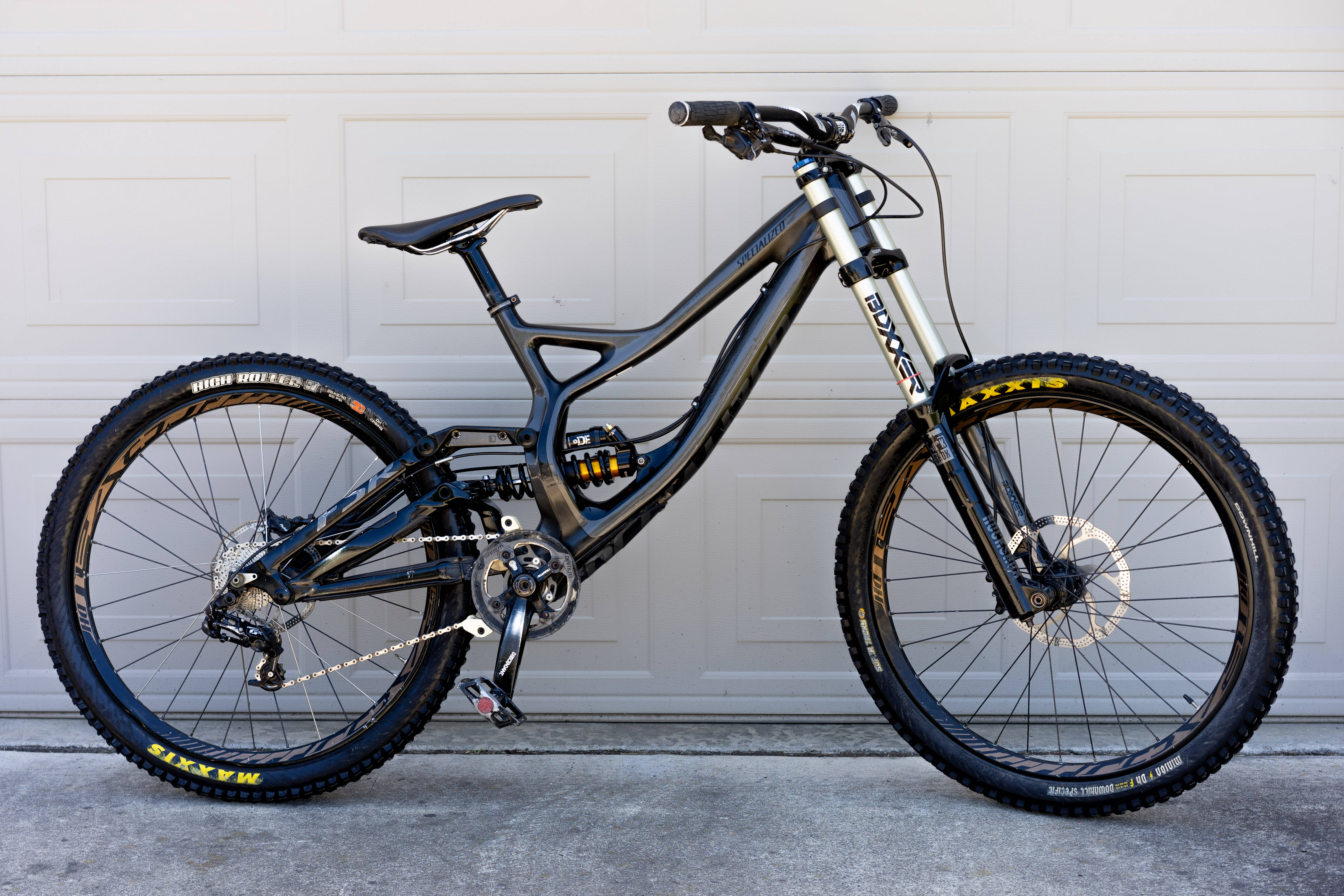 Mountain Bike 桌布 壁紙 — 一台時尚的黑色全避震登山車，配備黃色Maxxis輪胎，停在白色車庫門前。