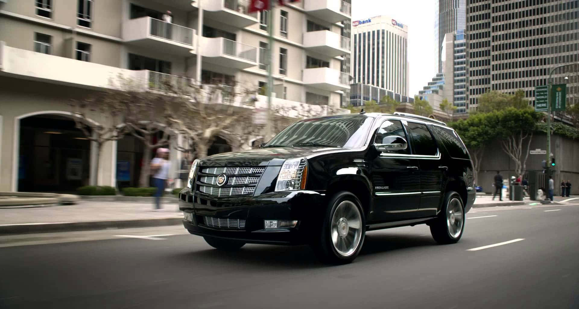Cadillac Escalade 桌布 壁紙 — 一台時尚的黑色凱迪拉克凱雷德SUV在繁華的城市街道上行駛，街道兩旁是現代建築和行人。