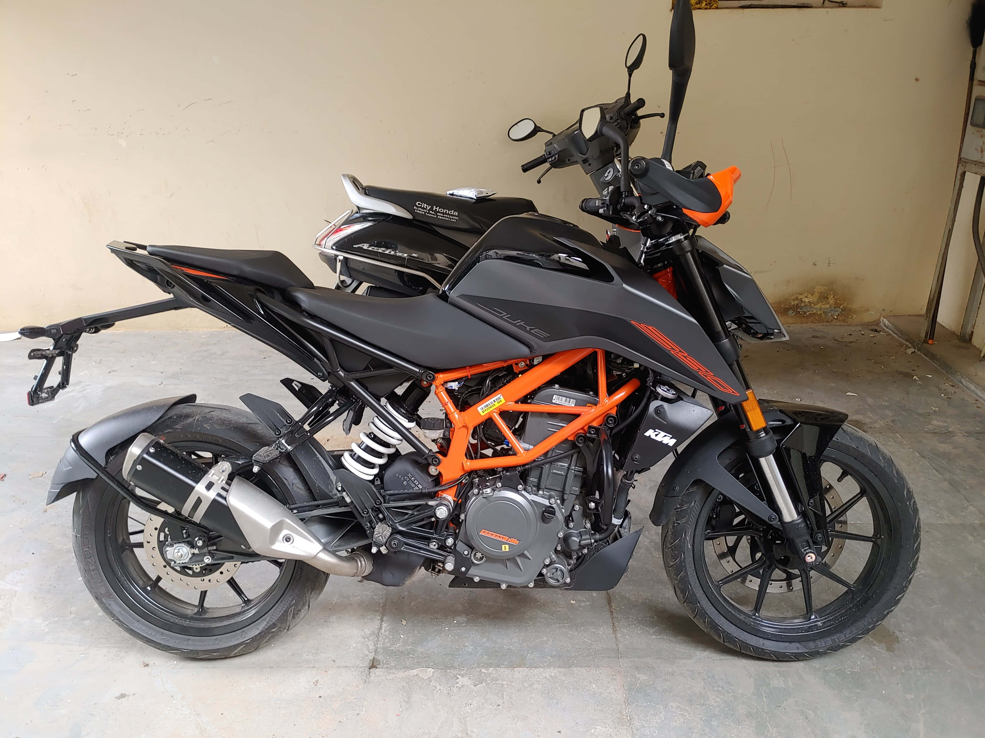 Garage 桌布 壁紙 — 一台時尚的黑色和橙色KTM Duke摩托車停放在室內混凝土車庫地板上，背景是純色米色牆壁。