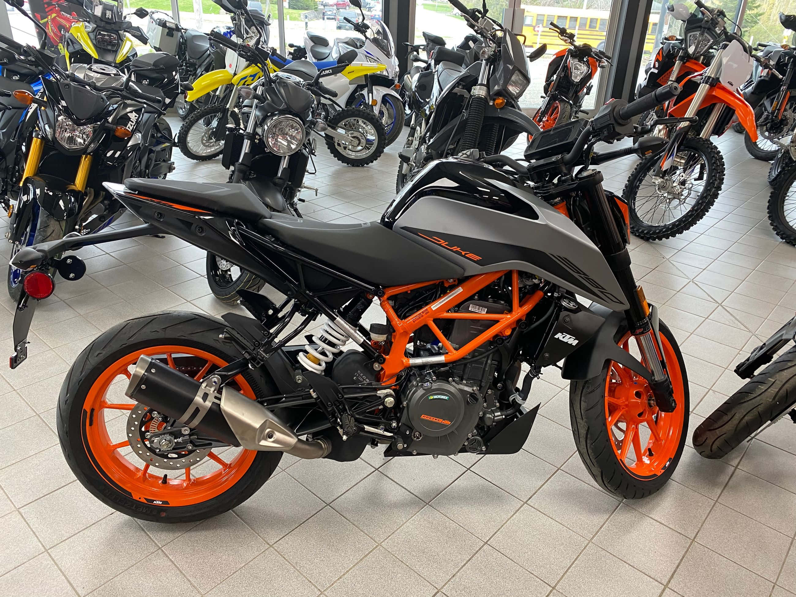 機車 桌布 壁紙 — 一台時尚的黑色和橙色KTM Duke摩托車在明亮的經銷商處展示，背景有其他摩托車。