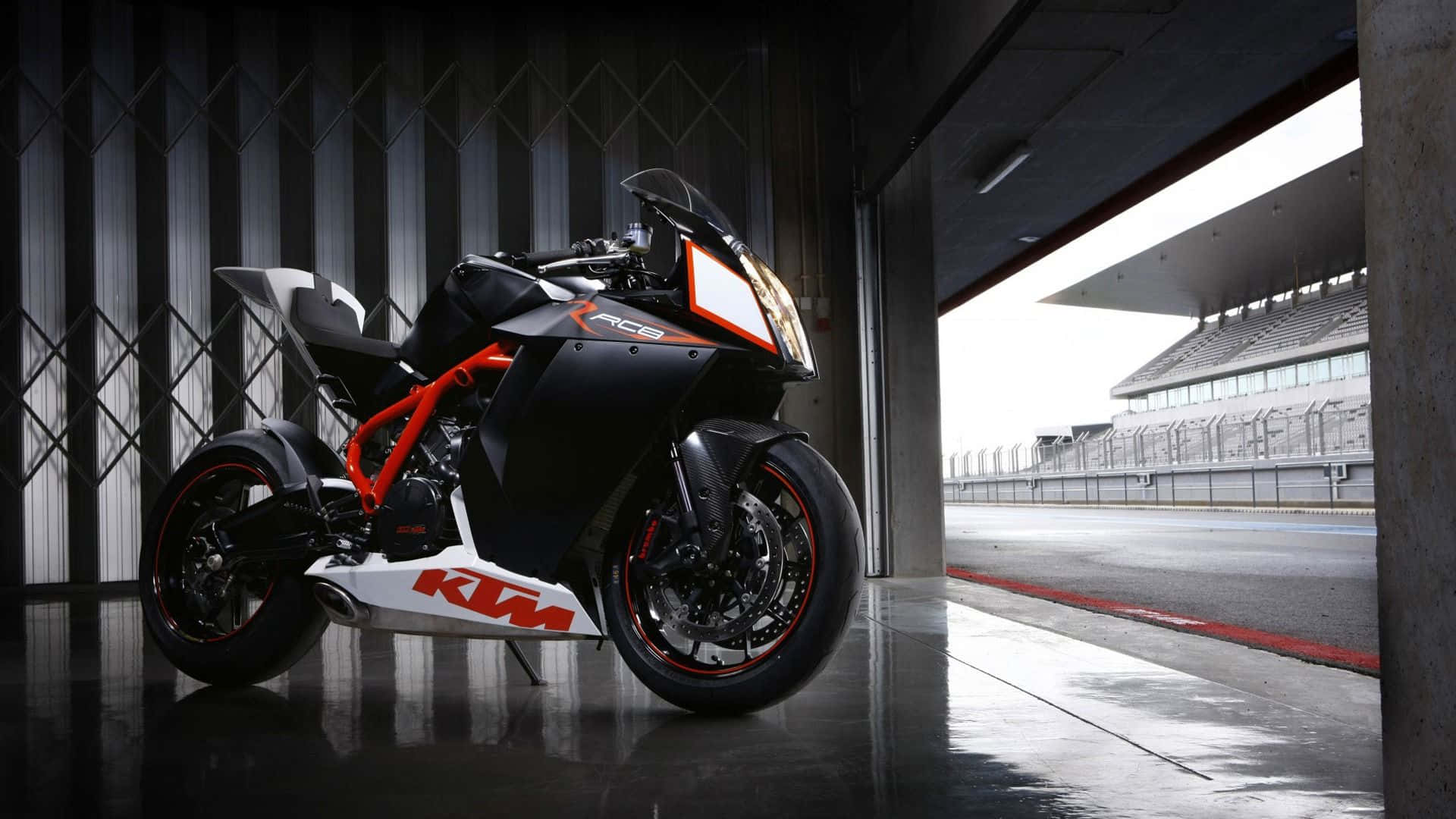 機車 桌布 壁紙 — 一台時尚的黑色和橙色KTM RC125機車停在車庫門口，俯瞰空蕩蕩的賽道。