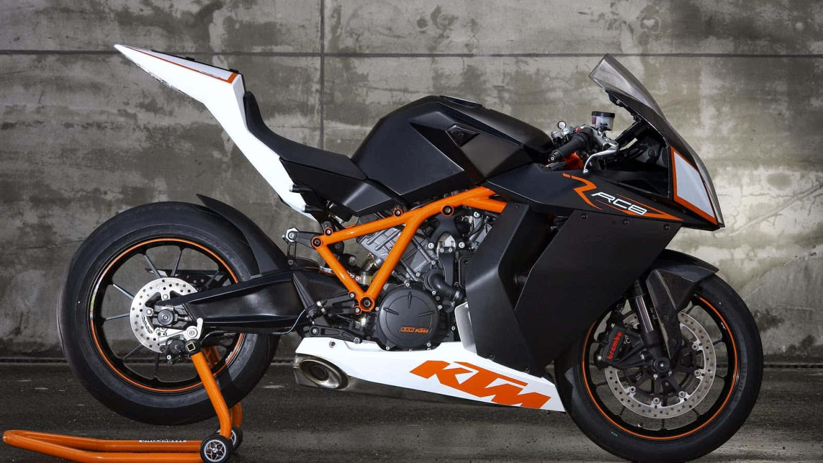 腳踏車 桌布 壁紙 — 一台時尚的黑色和橙色KTM RC8運動摩托車，停在風化的混凝土牆前。