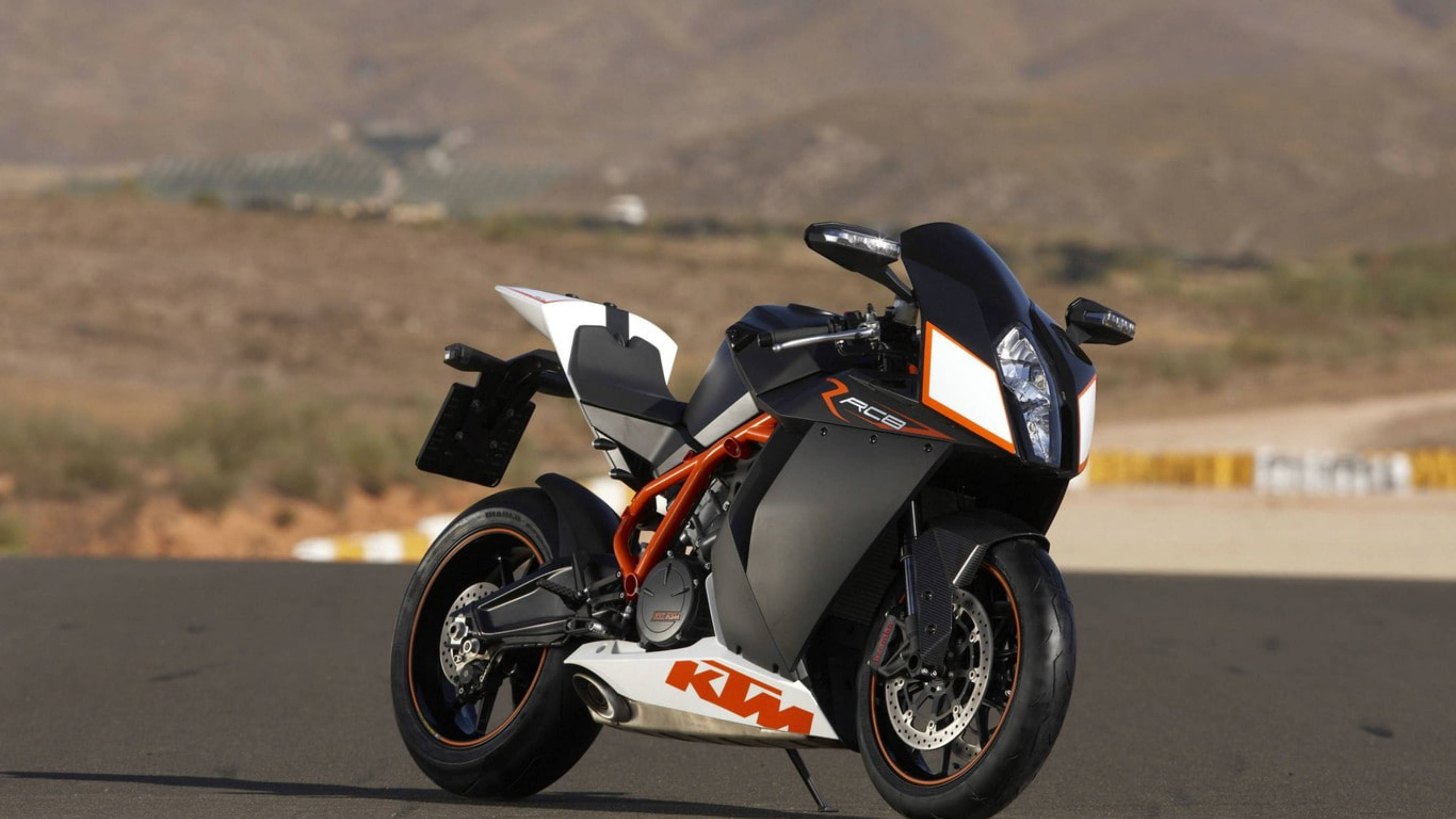機車 桌布 壁紙 — 一台時尚的黑色和橙色KTM RC8運動摩托車停在瀝青賽道上，背景是乾燥的山丘。