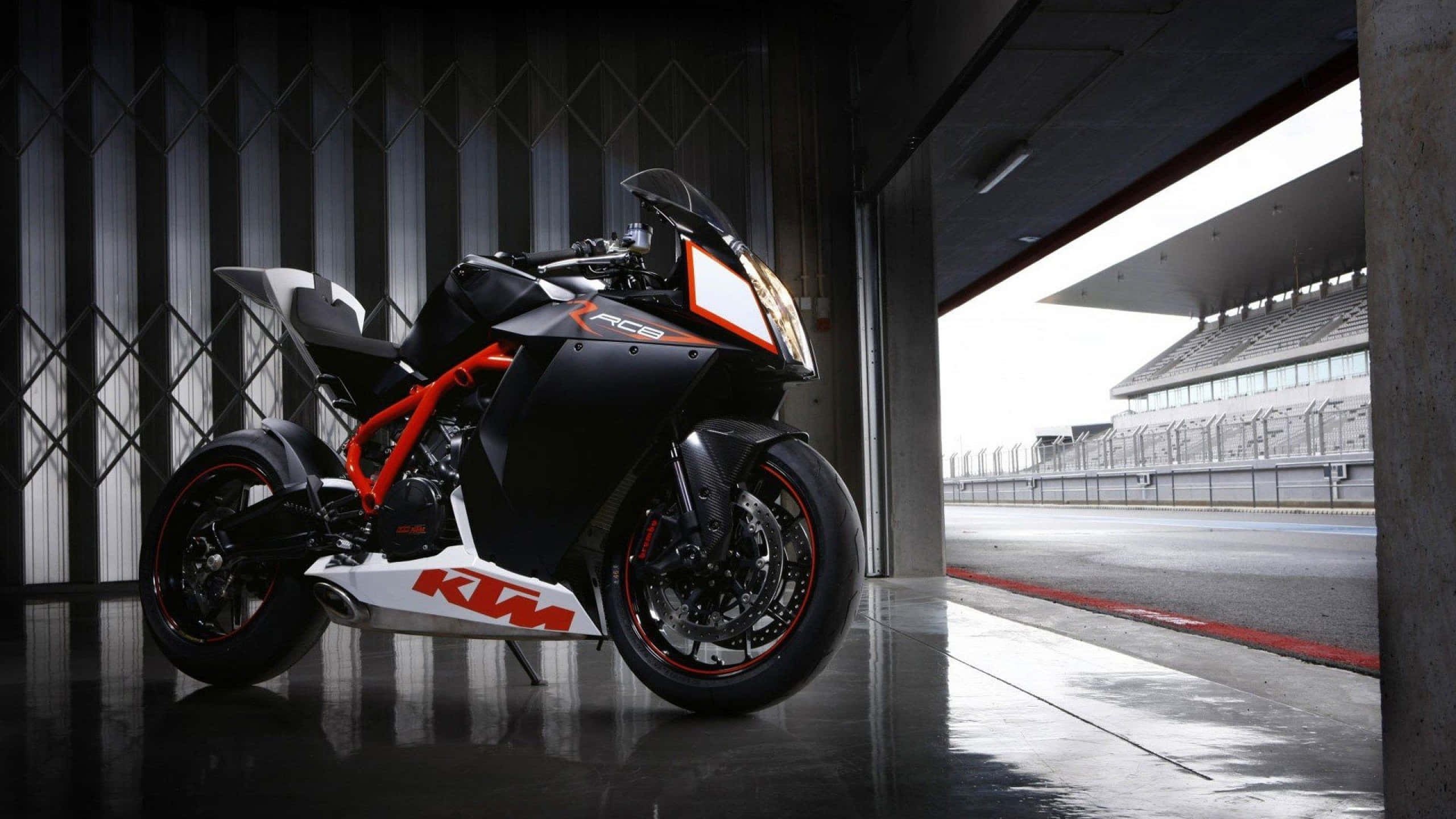motorbike 桌布 壁紙 — 一台時尚的黑色和橙色KTM RC8R機車停在車庫門口，外面可見賽道。
