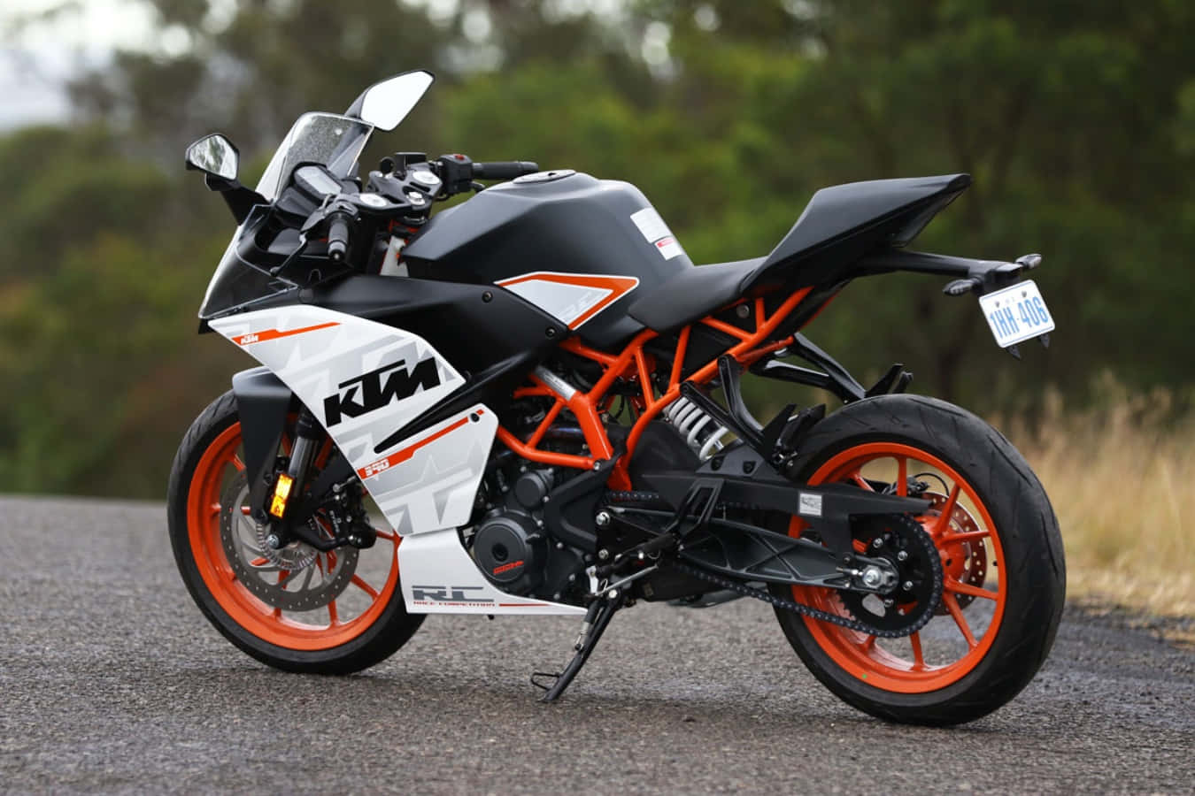 機車 桌布 壁紙 — 一台時尚的黑色和橙色KTM RC 250機車停在碎石路上，背景有模糊的綠色樹木。