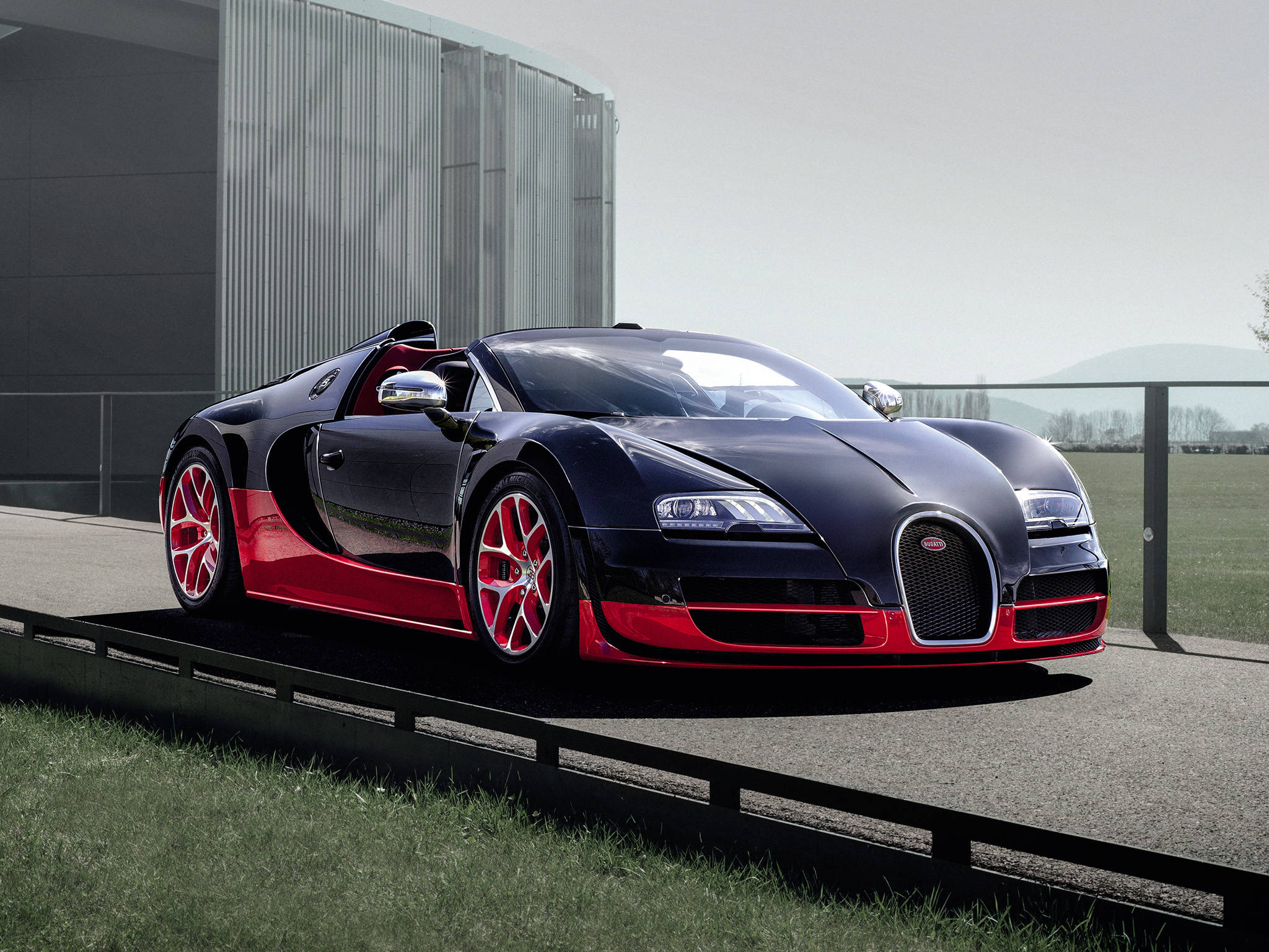 bugatti iPhone 桌布 壁紙 — 一台時尚的黑色和紅色Bugatti Veyron超級跑車停泊在草地旁邊的鋪砌平台上，背景是一座現代建築。