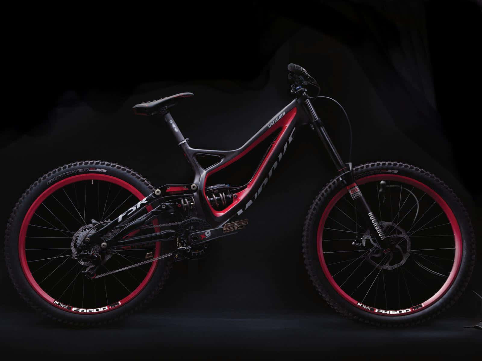 Mountain Bike 桌布 壁紙 — 一台時尚的黑色和紅色全避震登山車，配備紅色輪圈，在黑暗的攝影棚背景下戲劇性地矗立。
