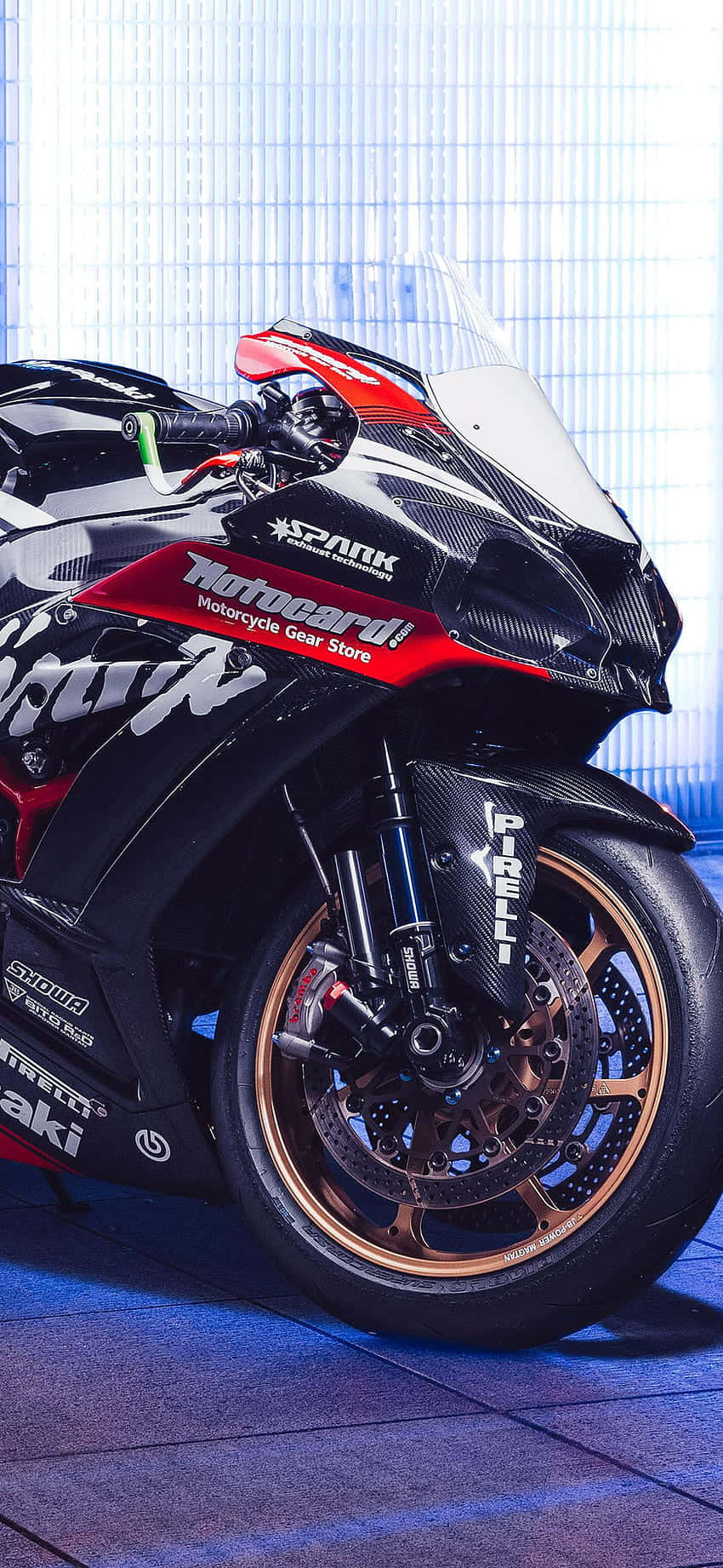 Superbike 桌布 壁紙 — 一台時尚的黑色和紅色運動機車，配備金色輪圈和贊助商貼紙，在明亮的燈光下於室內展示。