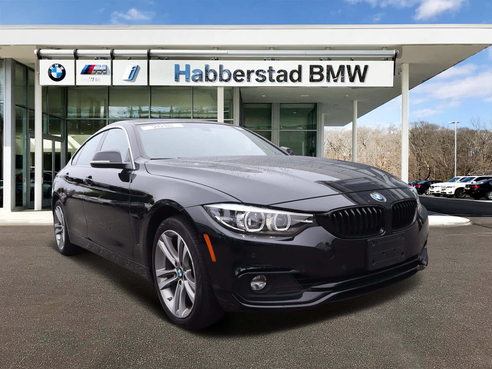 Bmw 440i 桌布 壁紙 — 一台時尚的黑色寶馬轎跑車在明亮的日光下，於現代化經銷商前閃閃發光，背景是光禿禿的樹木。