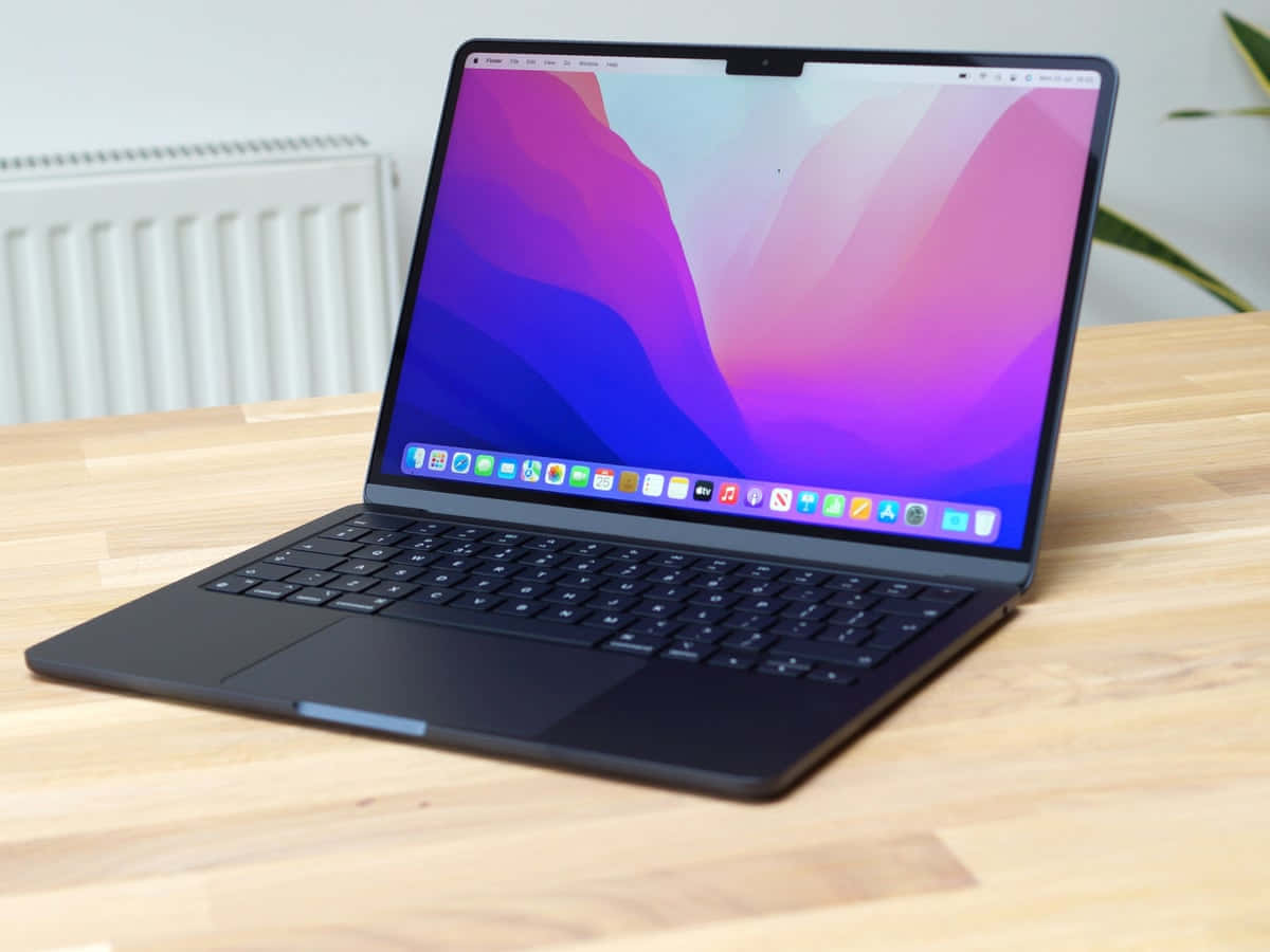 Black Macbook 桌布 壁紙 — 一台時尚的黑色筆記型電腦，帶有充滿活力的紫色和藍色抽象桌布，打開放在淺色木桌上。