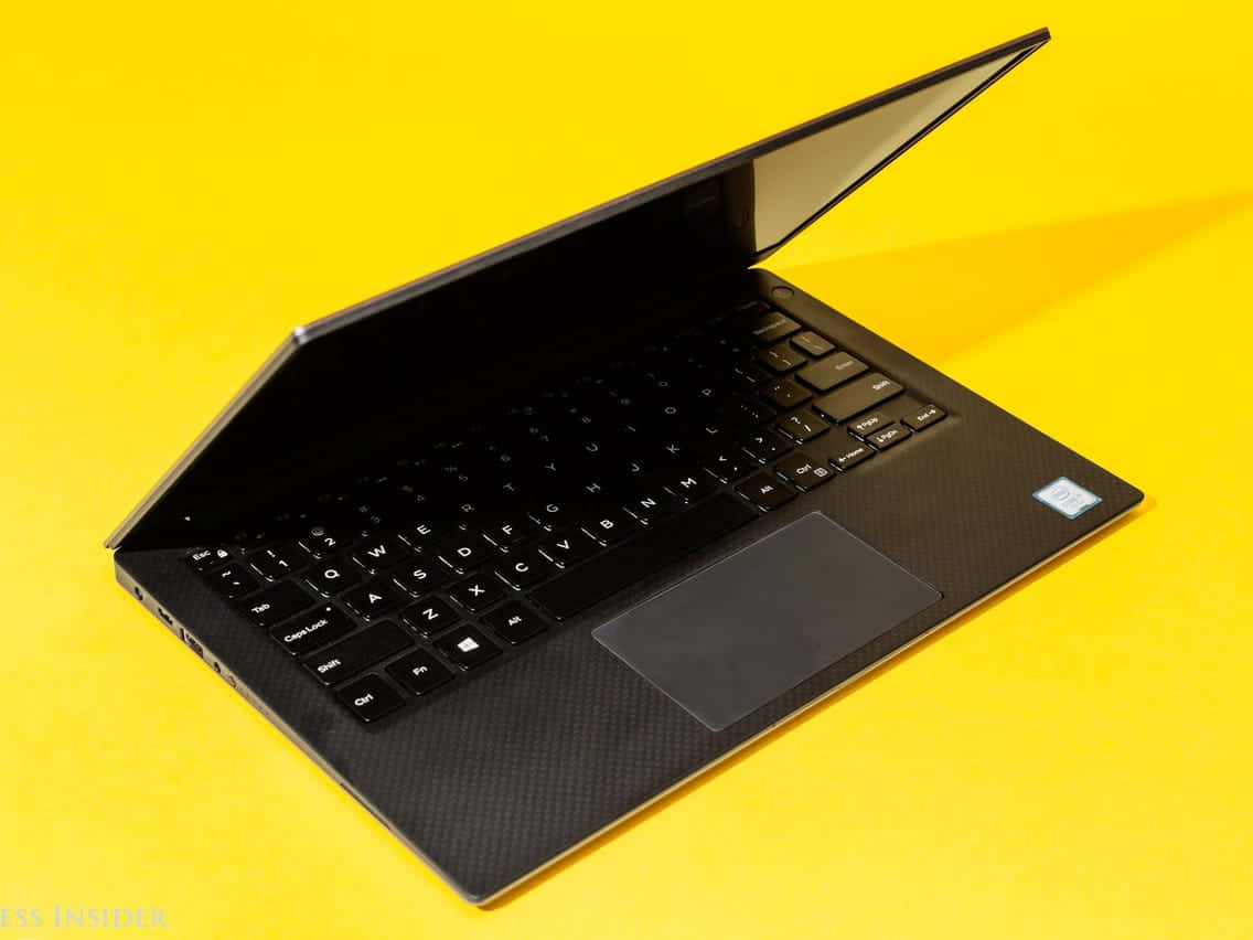 Dell 桌布 壁紙 — 一台時尚的黑色筆記型電腦，帶有碳纖維紋理，打開放在鮮黃色背景上。