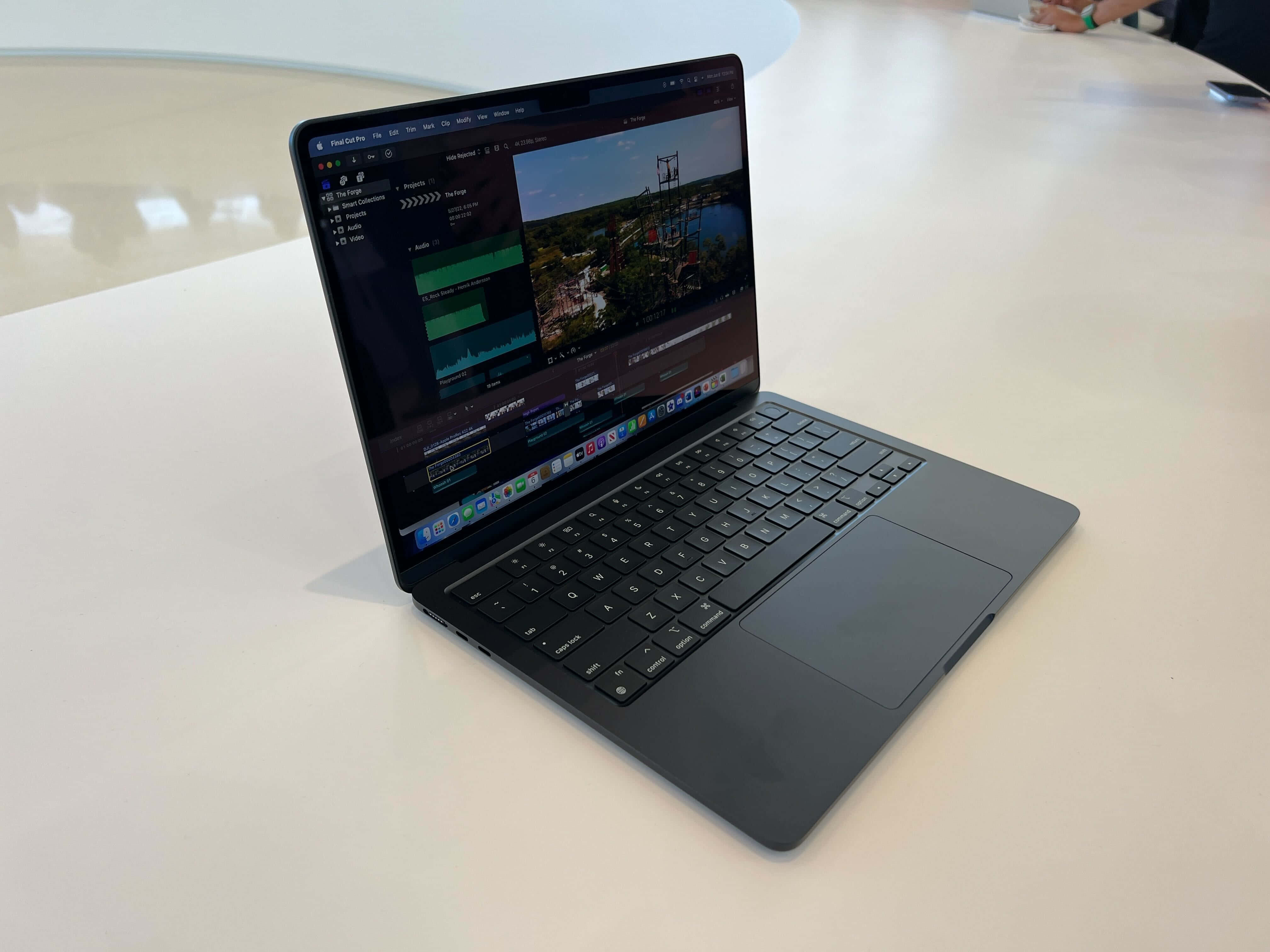 Black Macbook 桌布 壁紙 — 一台時尚的黑色筆記型電腦打開放在白色桌子上，顯示一個帶有風景戶外剪輯的影片編輯介面。