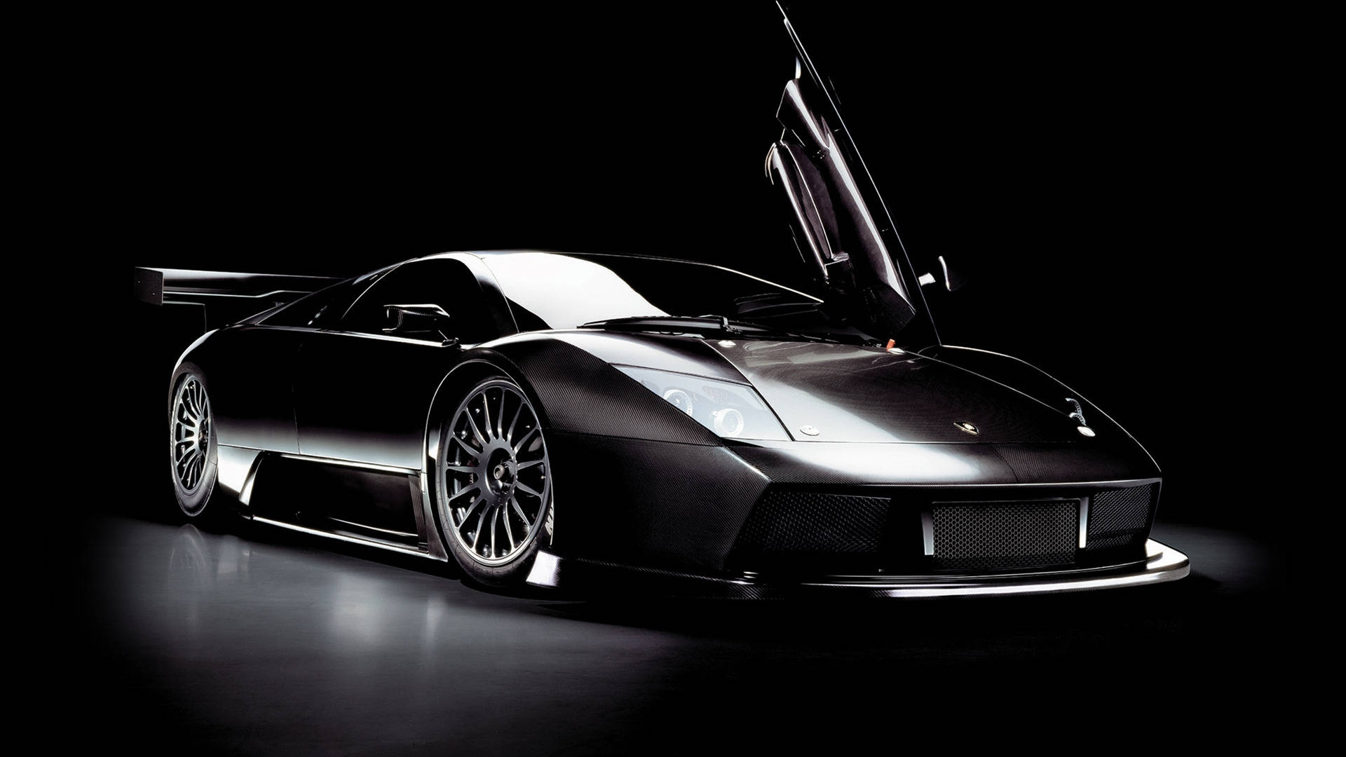 Lamborghini 4K 桌布 壁紙 — 一台時尚的黑色藍寶堅尼跑車，剪刀門打開，在黑暗背景下被戲劇性的工作室燈光照亮。