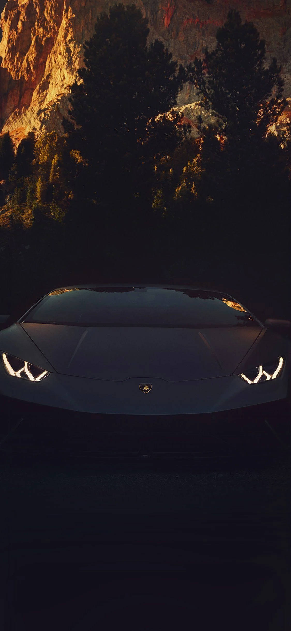 Luxury 桌布 壁紙 — 一台時尚的黑色藍寶堅尼跑車在黃金時段，以銳利的車頭燈照亮黑暗的森林峽谷。