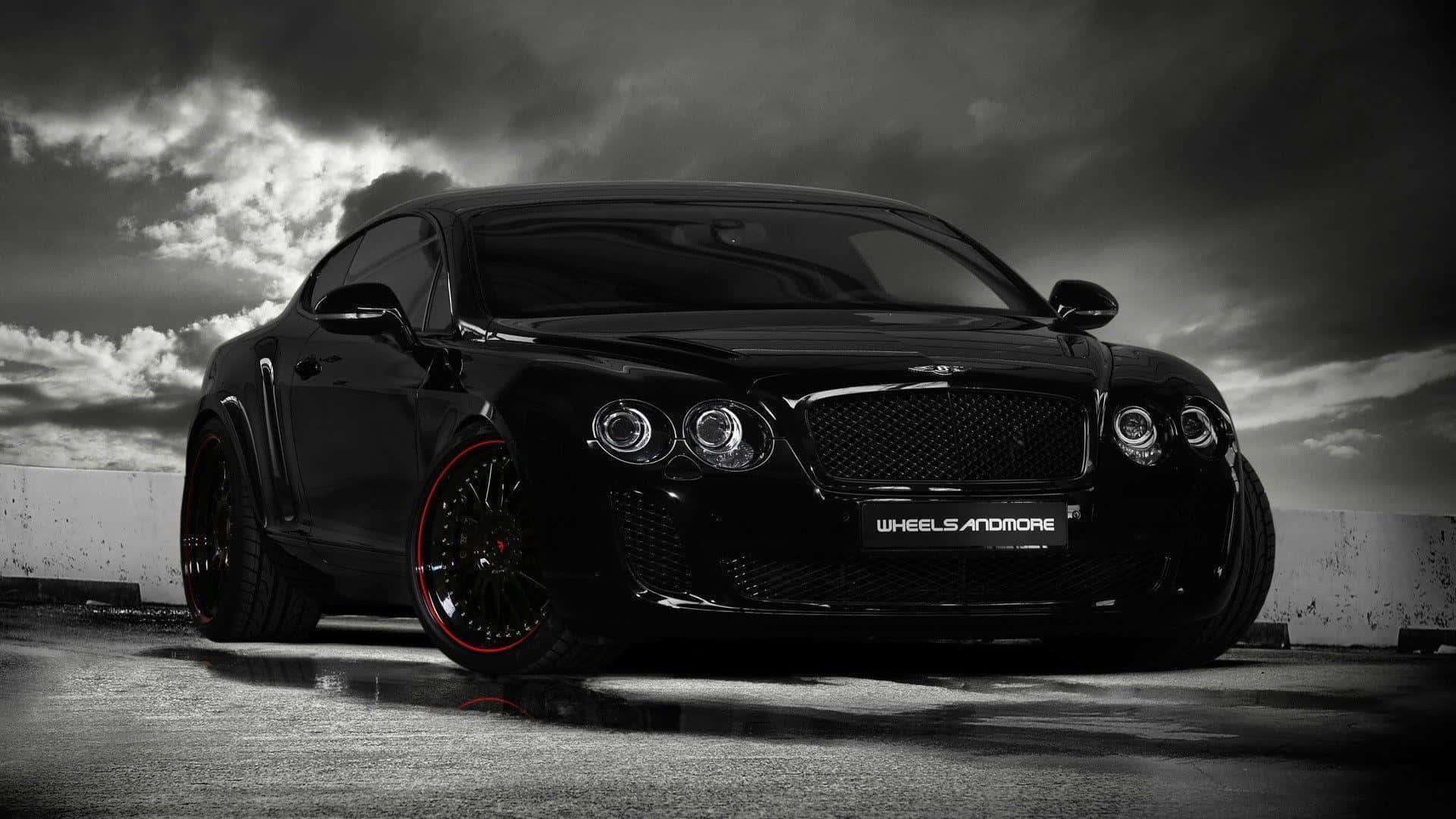 Black Car 桌布 壁紙 — 一台時尚的黑色賓利 Continental GT 配備紅色點綴輪圈，在戲劇性的暴風雨天空下，靜立在濕漉漉的混凝土路面上。