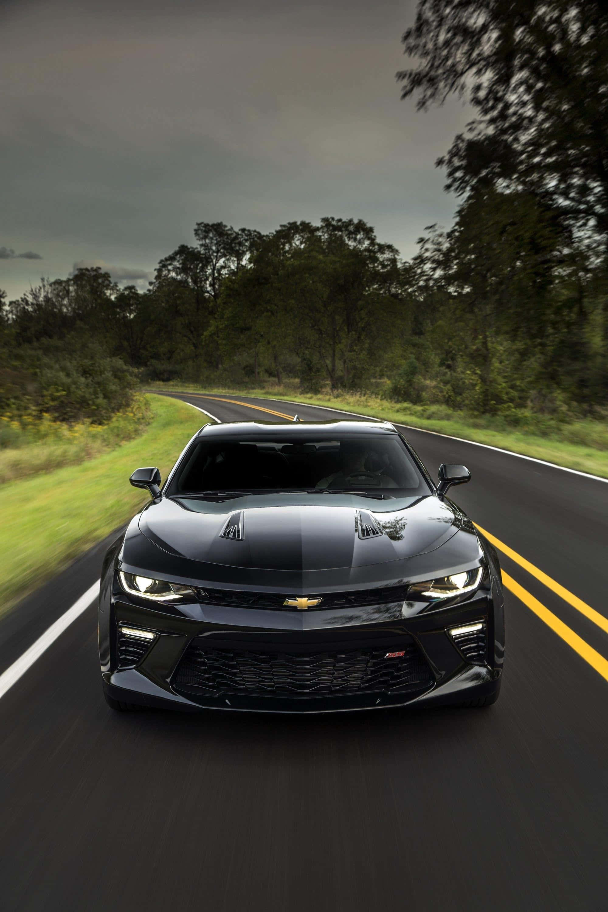 Chevrolet 桌布 壁紙 — 一台時尚的黑色雪佛蘭Camaro SS在陰天之下，沿著兩旁綠樹成蔭的蜿蜒鄉村道路飛馳。