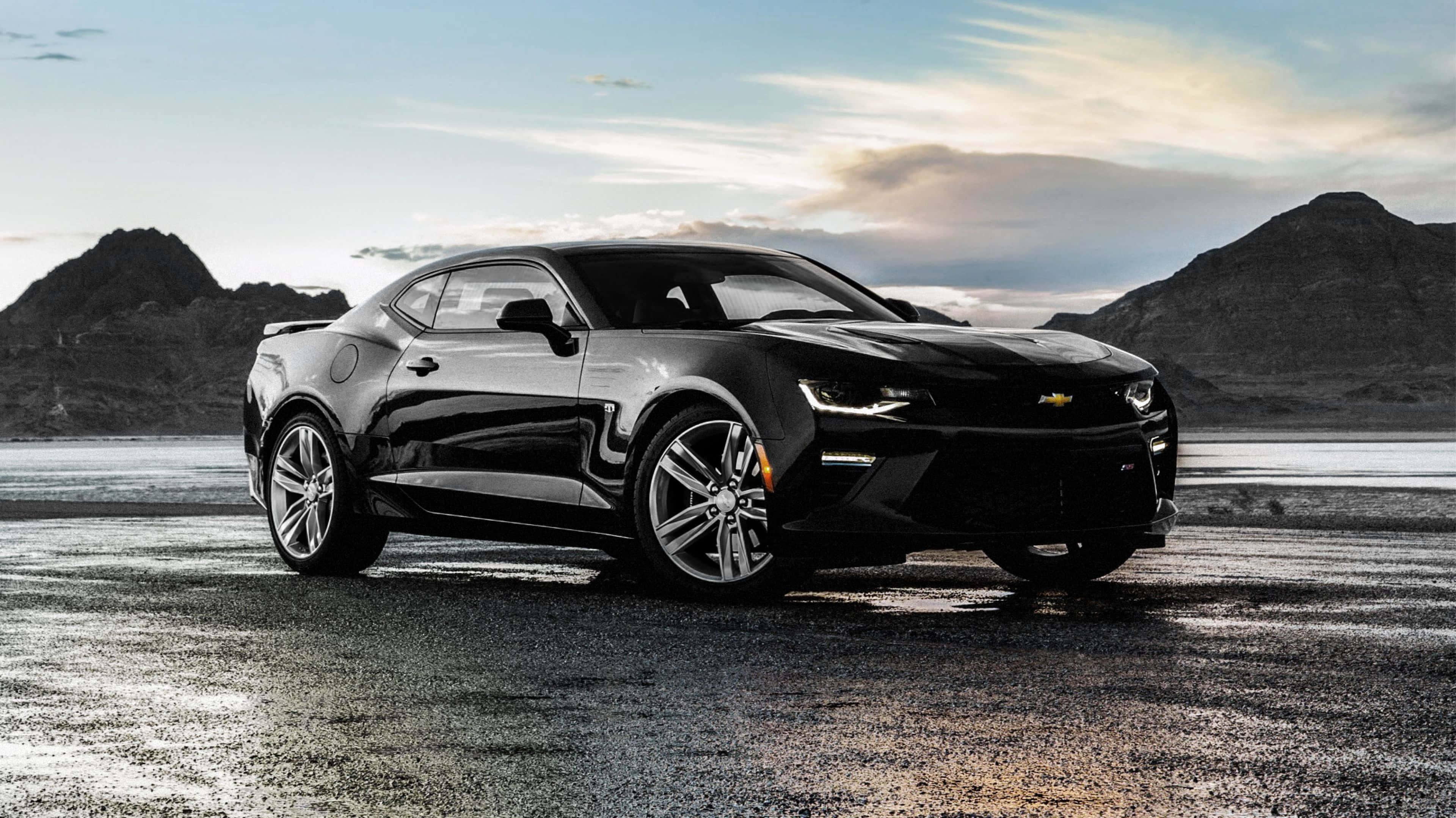 Cool Camaro 桌布 壁紙 — 一台時尚的黑色雪佛蘭Camaro跑車在潮濕的沙漠公路上閃耀，背景是崎嶇的山脈，天空柔和暮色。