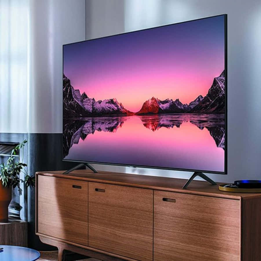 tv 桌布 壁紙 — 一台時尚電視顯示出日落時分壯麗的山湖景色，鮮豔的粉紅色和紫色色調完美地倒映在平靜的水面上。