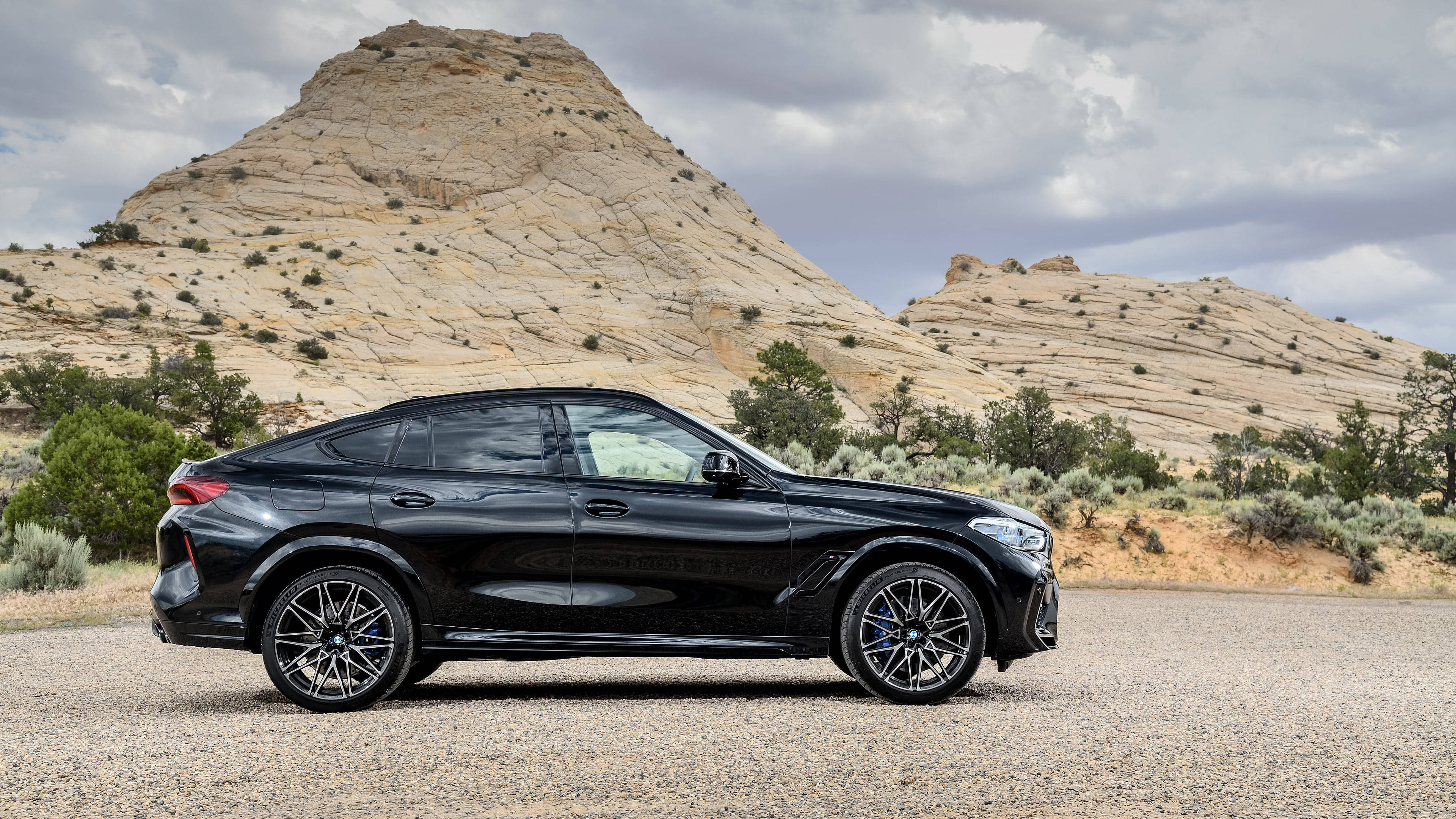 m 桌布 壁紙 — 一台時尚黑色BMW X6 SUV停放在碎石上，背景是崎嶇的岩石山丘和陰天。