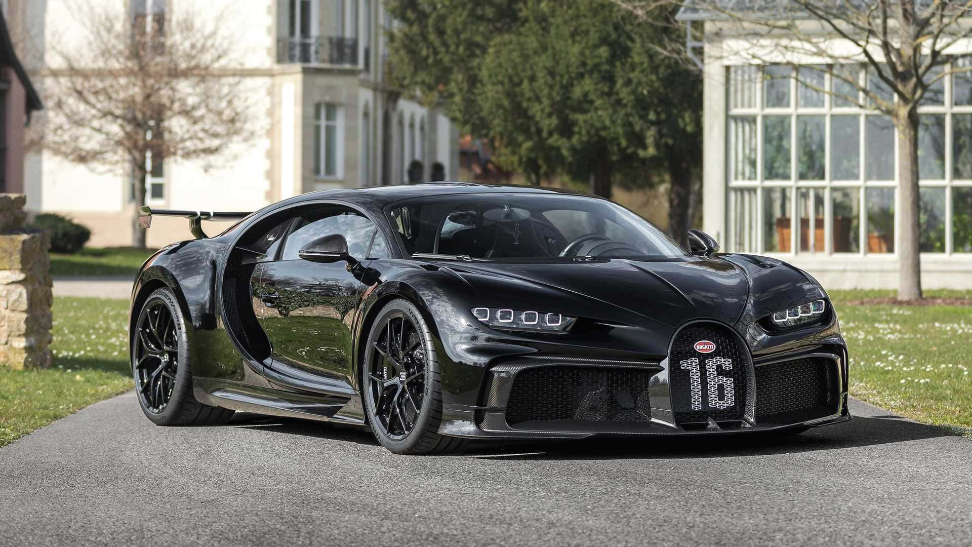 桌布 壁紙 — 一台時尚黑色Bugatti Chiron Super Sport 300+停在鋪砌車道上，剪刀門敞開，周圍是修剪整齊的草坪和優雅房屋，在明亮日光下。